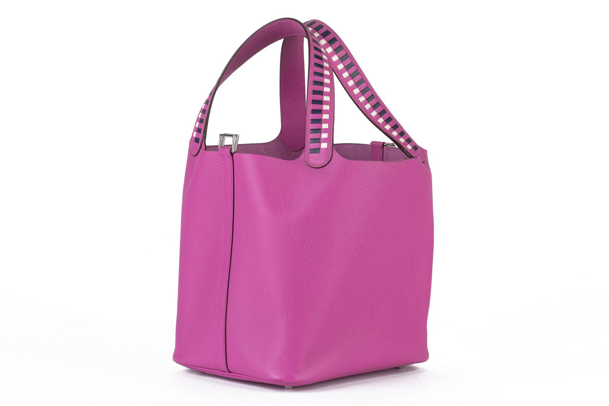 Ce Tressage De Cuir Picotin Lock 22 PM en Magnolia, Bleu Saphir et Craie est réalisé en cuir d'epsom de couleur rose. Les poignées tressées sont ornées d'une incrustation de cuir bleu et blanc. La sangle supérieure se déverrouille et s'ouvre sur un