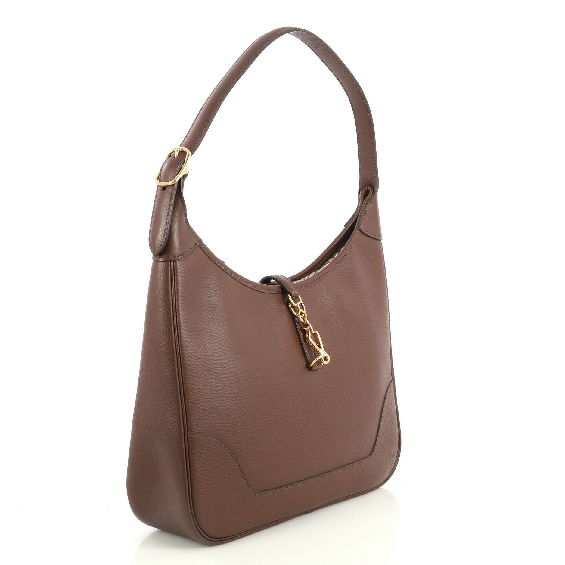 This Hermes Trim II Bag Ardennes 31, crafted in Marron Fonce brown Ardennes leather, features looped shoulder strap and gold hardware. Its clasp closure opens to a Marron Fonce brown raw leather interior with side zip and slip pockets. Date stamp
