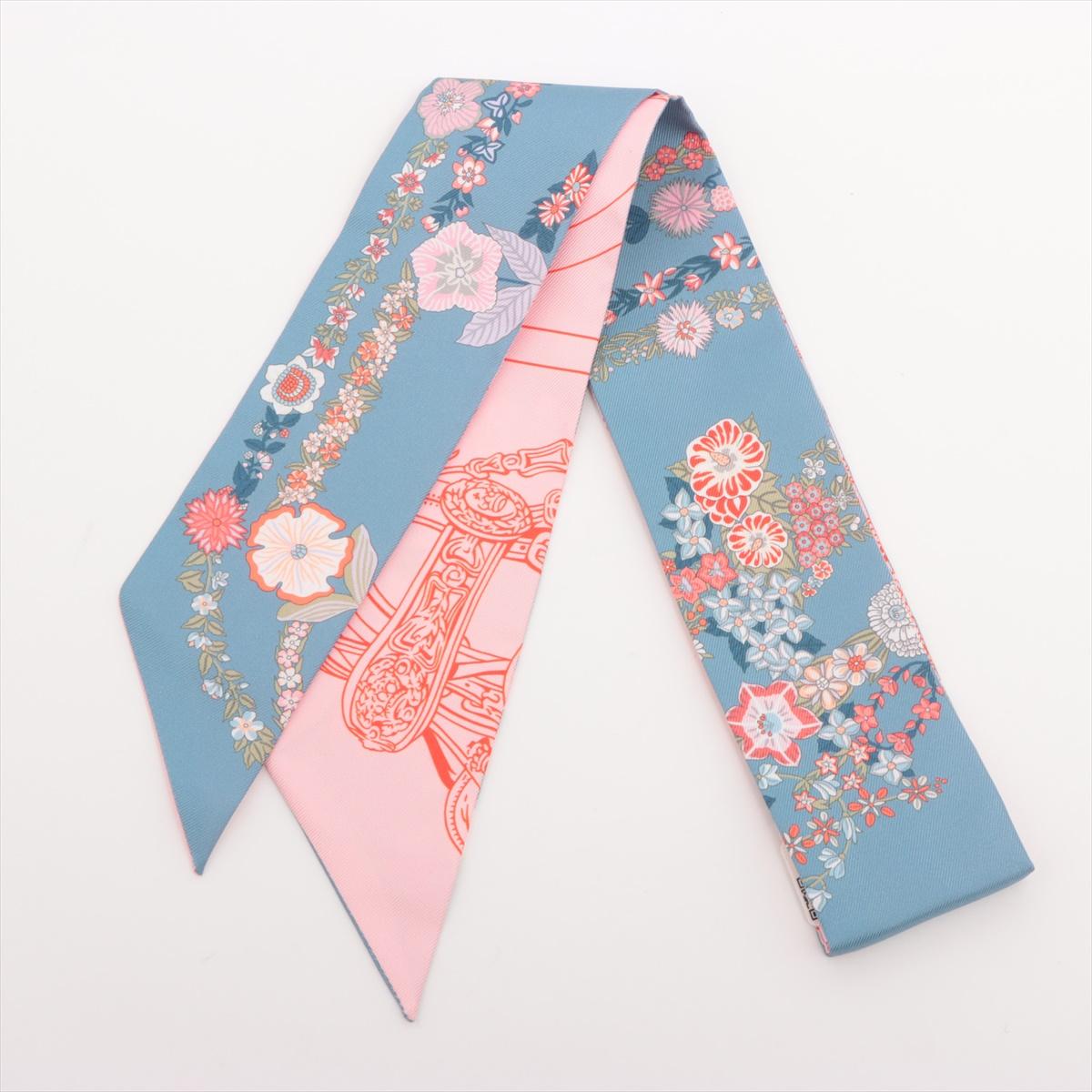 The Hermès Twilly Brides De Gala En Fleurs Silk in Blue Jean x Pink is a refined and artistic accessory that reimagines the classic Brides De Gala motif with a delicate floral twist. Crafted from luxurious silk, the Twilly features