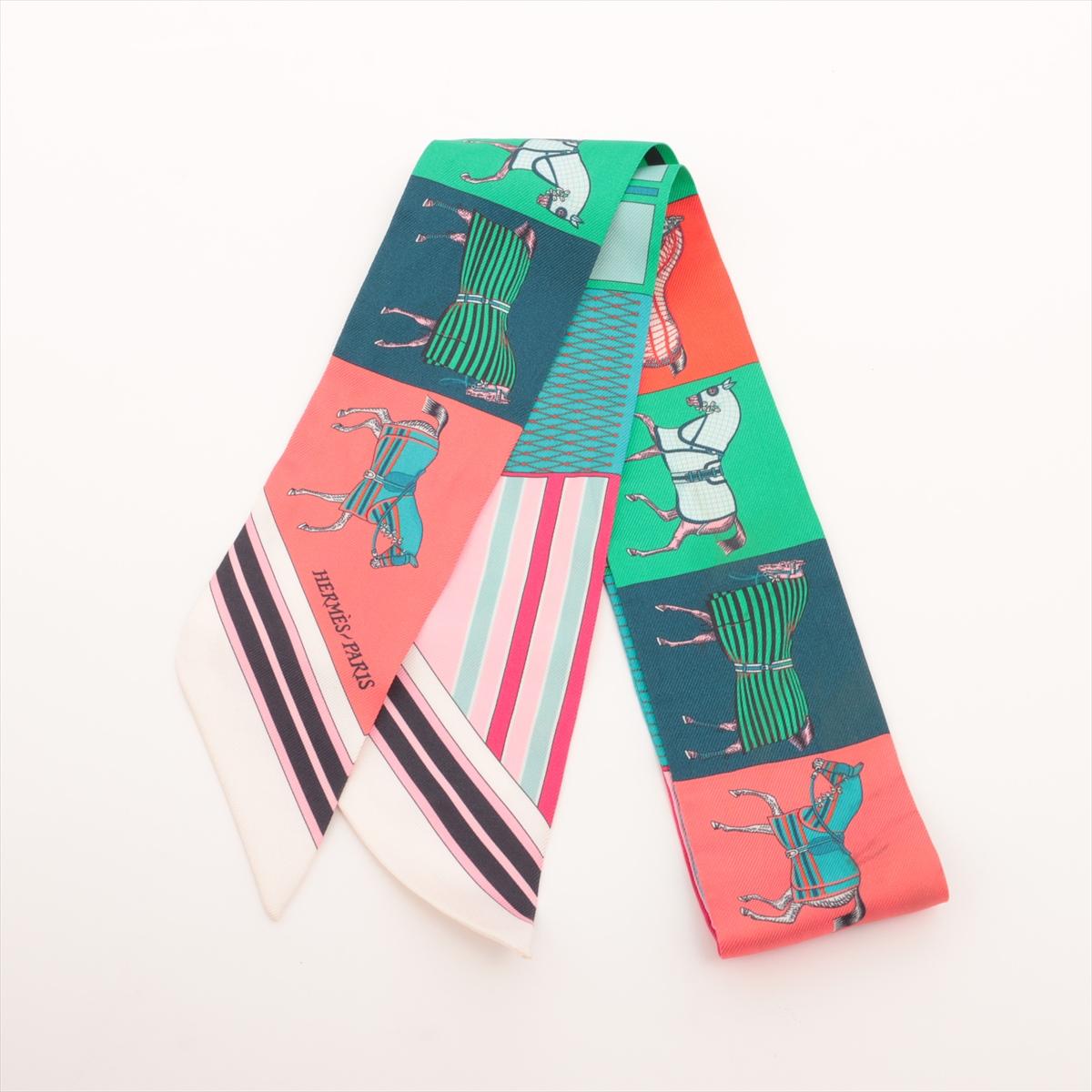 The Hermès Twilly Couvertures Nouvelles in Multicolor Pink x Green is a vibrant and playful accessory that captures the brand’s equestrian heritage with a modern twist. Crafted from luxurious silk, the slender scarf features the Couvertures