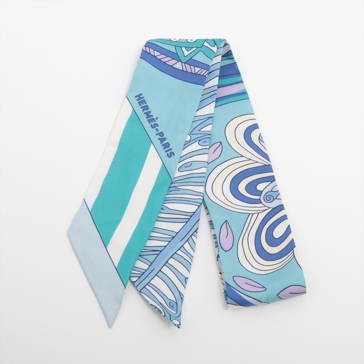 The Hermès Twilly Le Jardin De La Maharani in Cyan is a delicate and enchanting silk accessory inspired by the opulence of royal gardens. Designed with intricate floral motifs and ornamental details, the pattern reflects a fusion of cultural