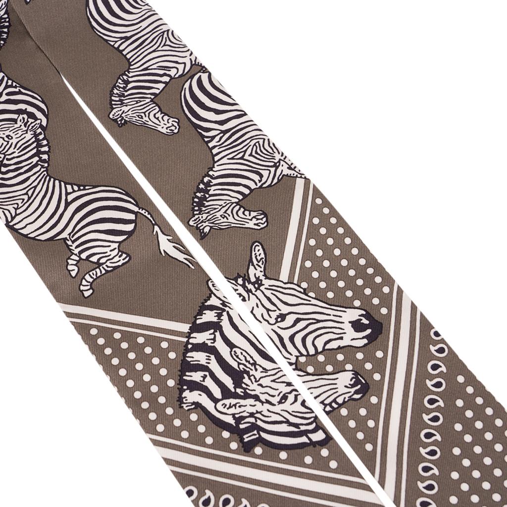 Guaranteed authentic Hermes Twilly features Set of 2 Les Zebres in Gris Taupe and Noir.
Black and White Zebras against the Gris Taupe background.
Designed by Robert Dallet.
This iconic Hermes accessory can be worn in a myriad ways to add a playful