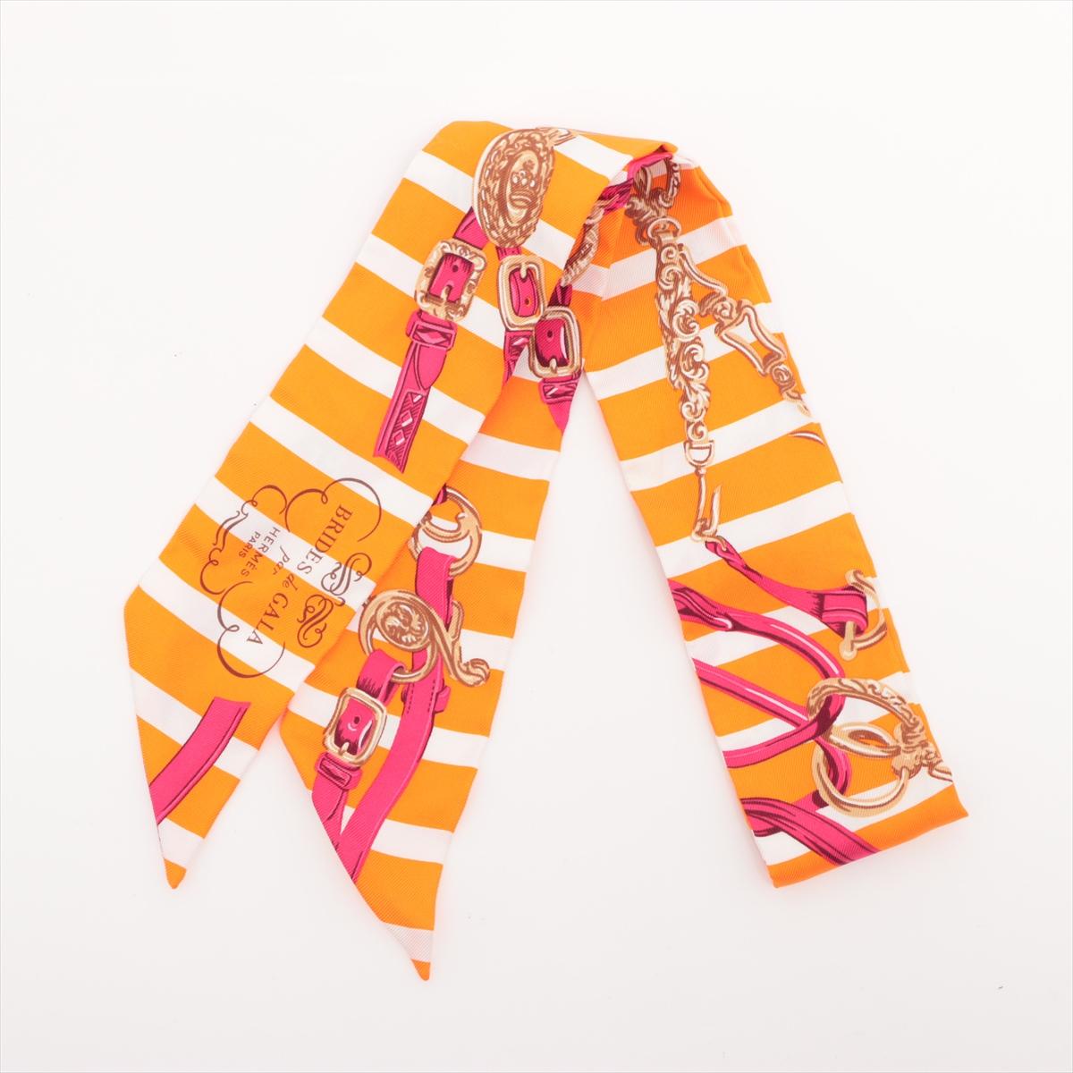 The Hermès Twilly Brides de Gala Stripes in Orange x White is a striking and sophisticated silk accessory that reinterprets a classic house motif with a fresh, graphic twist. Featuring the iconic Brides de Gala equestrian design, the version is set