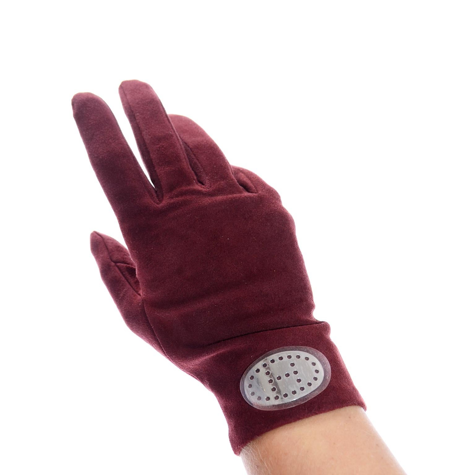 These are burgundy red reindeer leather gloves designed by Hermés. They have a silver plate at the top of the wrist that is silver with a pierced H in the center. The plates still have the plastic film protecting the silver and the gloves were never