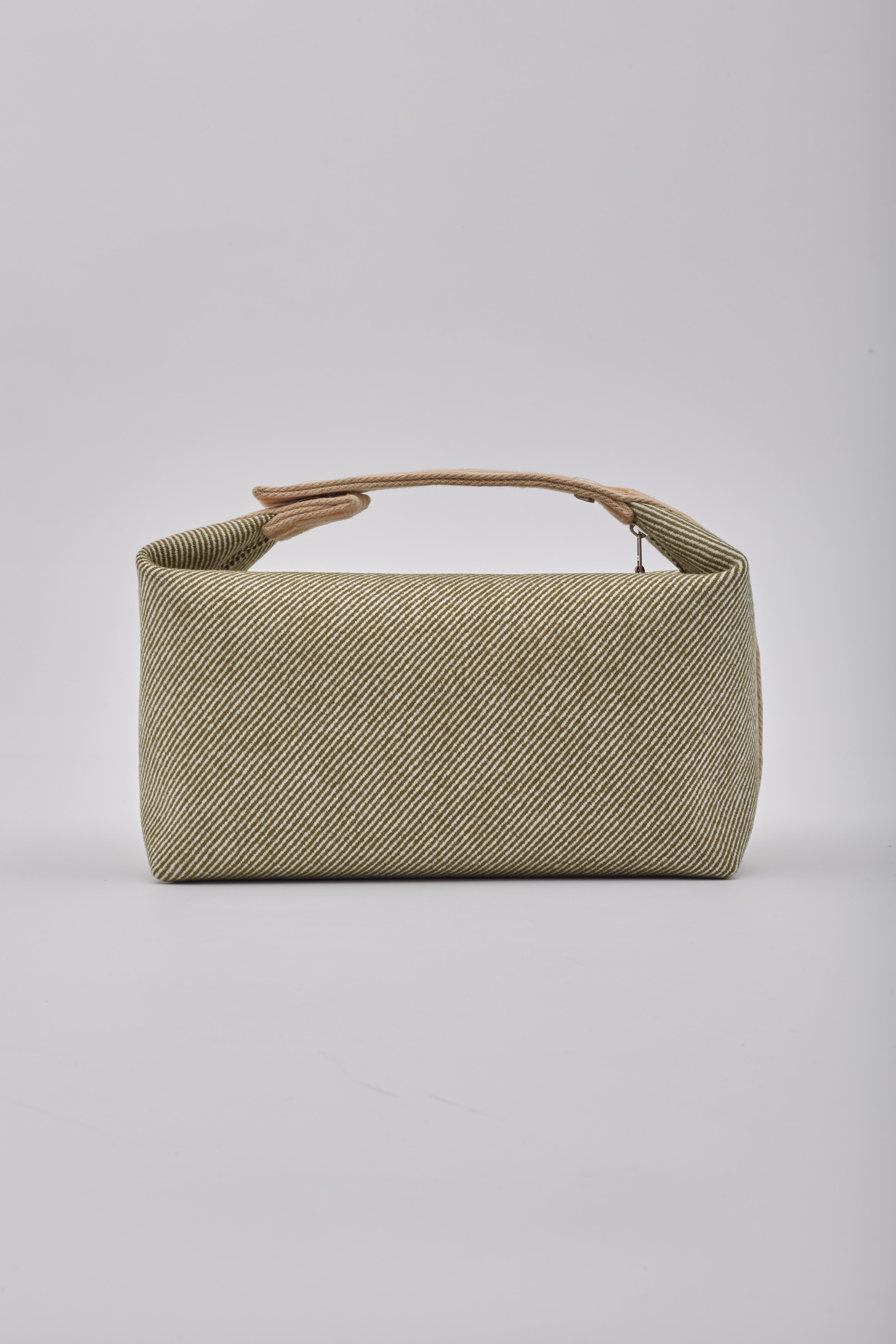 The pouch vanity bag is made of green wool and consists of a snap closure on the top handle, along with a yellow and beige checkerboard strap around the bag. The top zipper opens to a beige fabric interior with patch pockets.

Color: Forest