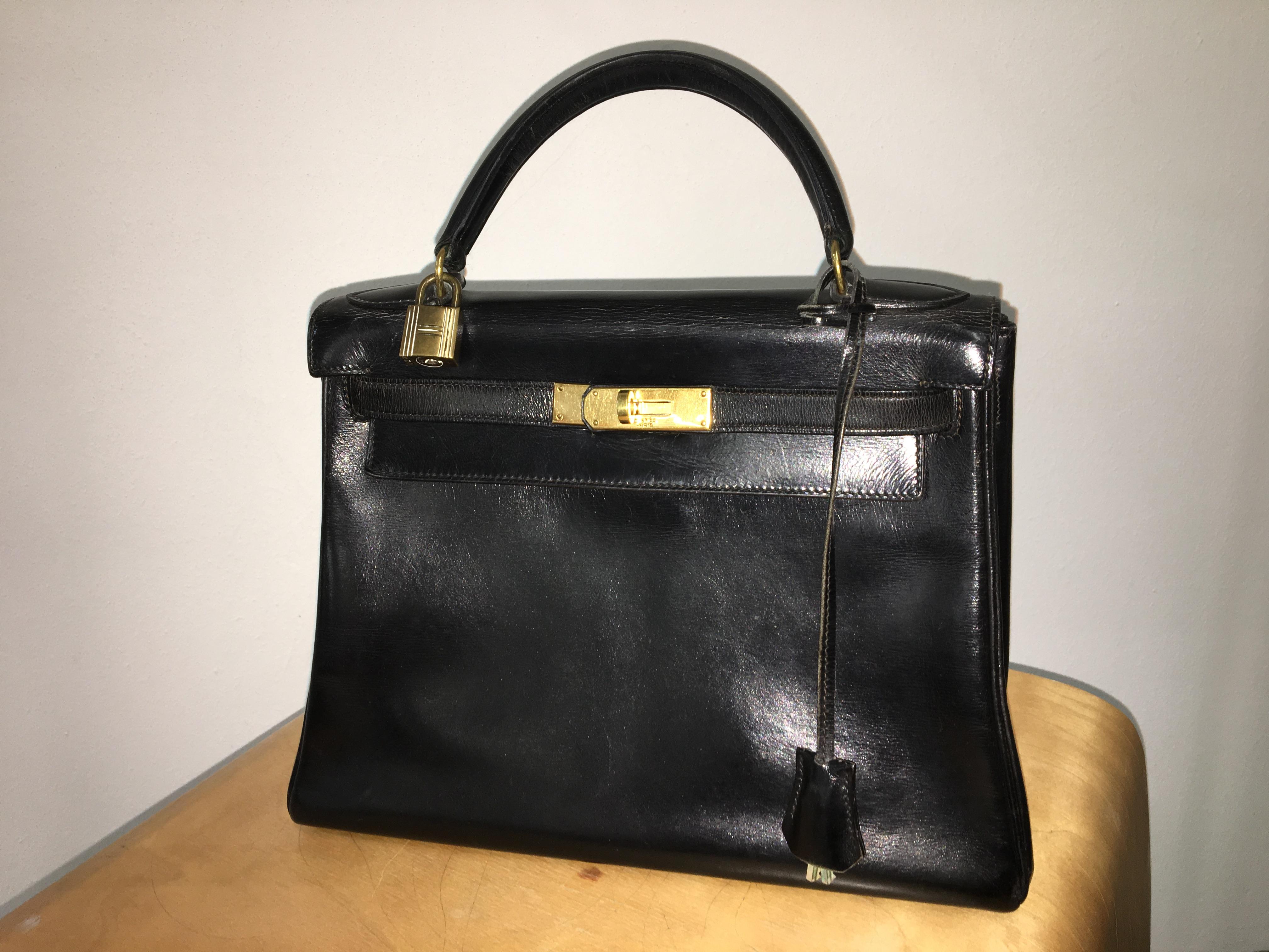Vintage black leather Kelly bag. Featuring a trapeze body, top flap closure with twist-lock strap fastening, gold-tone hardware, front embossed logo stamp, a detachable leather clochette, lock and two keys, single structured leather top handle.
