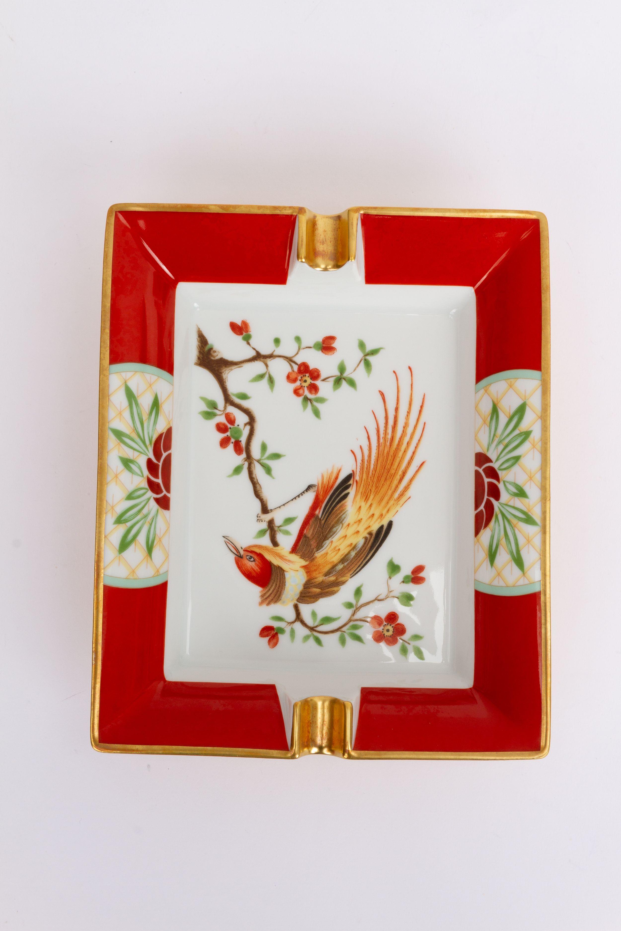 Hermès vintage Aschenbecher in rot. In der Mitte des Stücks befindet sich das Bild eines exotischen Vogels, der auf einer Blumenkette sitzt. Der Aschenbecher ist in ausgezeichnetem Zustand und wird mit der Originalverpackung geliefert.
