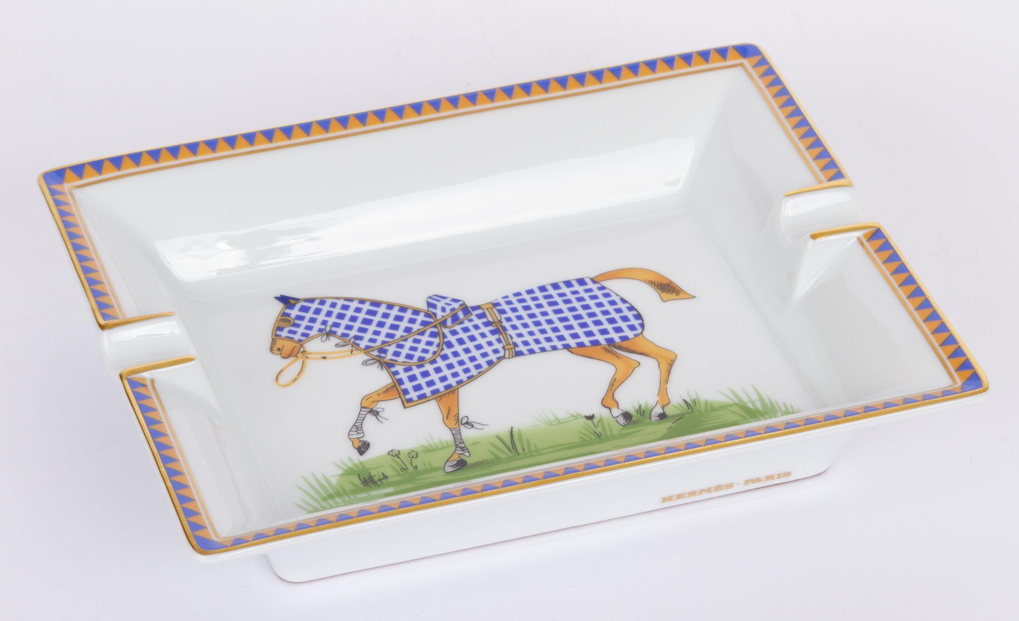 Hermès vintage ashtray in white. In the center is a print of a galloping horse covered in a blue blanket. The piece is in excellent condition and includes the original box.