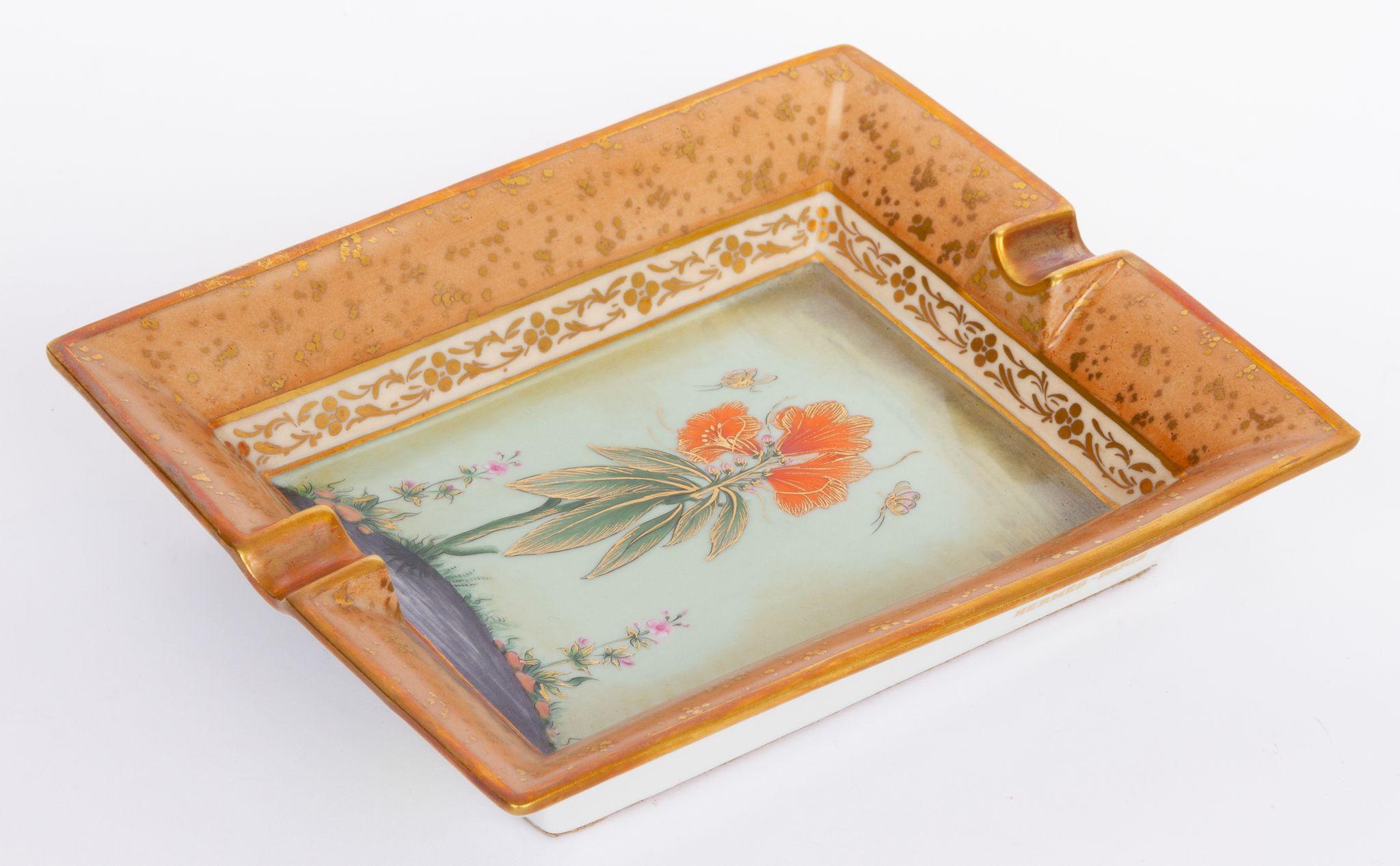 Hermès vintage ashtray in a beige golden tone. The center of the piece shows a red flower. And the edges are in a gold ornamental style. The ashtray is in excellent condition and comes with the original box.