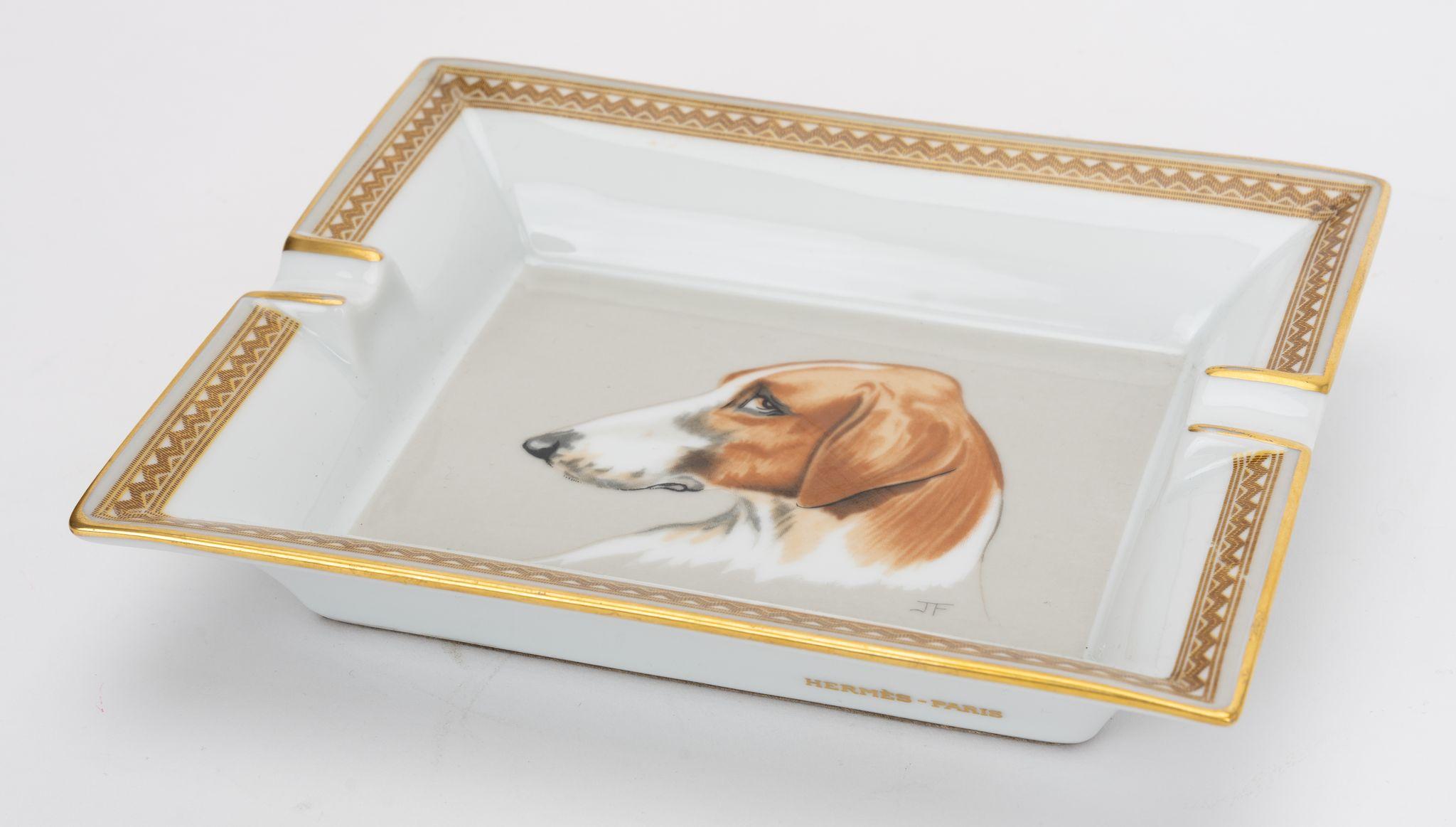 Hermès vintage ashtray in white. In the center is a print of a judgmental looking dog. Gold trim. The piece is in excellent condition