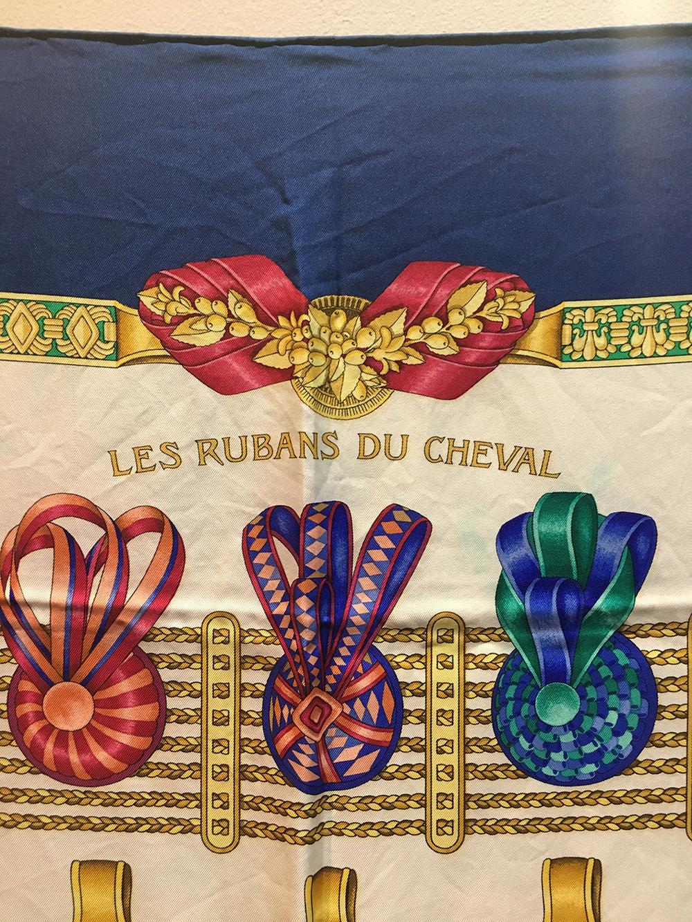 Beautiful Hermes vintage les Rubans du Cheval silk scarf in very good condition. Original silk screen design c1993 by Joachim Metz features a colorful array of equestrian ribbons over a white background with a blue border. 100% silk. hand rolled