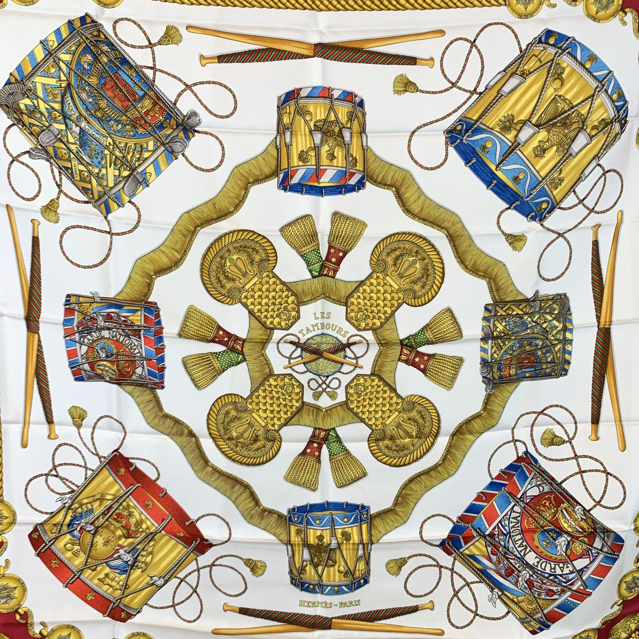 A March Through Time - Hermès 'Les Tambours' Scarf by Joachim Metz (1989) Step into the rhythm of elegance with Les Tambours, a striking Hermès silk carré designed by the celebrated Joachim Metz and first released in 1989. This vintage gem captures
