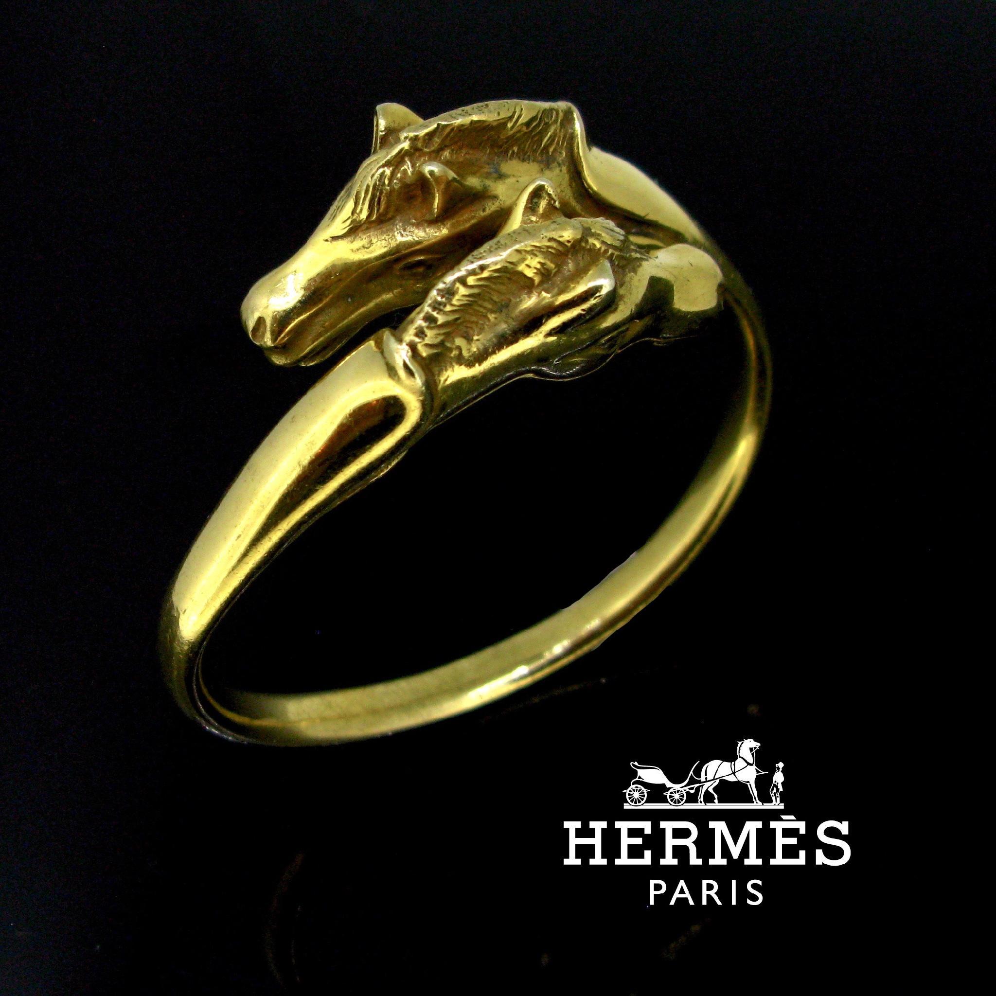 Weight:	96.59


Metal:	Gold Plated 


Condition:	Very Good


Signature:	Hermès Paris


Hallmarks:	Maker’s mark: R – clover – D for RAVINET D’ENFERT


Comments: 	This open bangle features two crossing horse heads. It is fully made in gold plated and