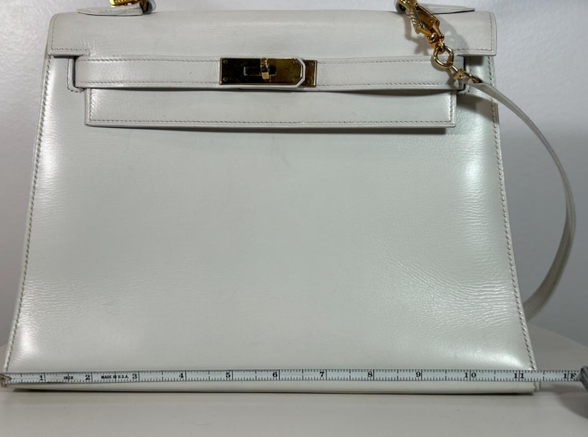 Bolso Hermès Kelly 28 blanco de piel de caja Circa 1967 con correa de piel desmontable. El bolso viene con la llave y el candado a juego para cerrarlo completamente. Está en muy buen estado, aparte de un ligero envejecimiento en el interior y el