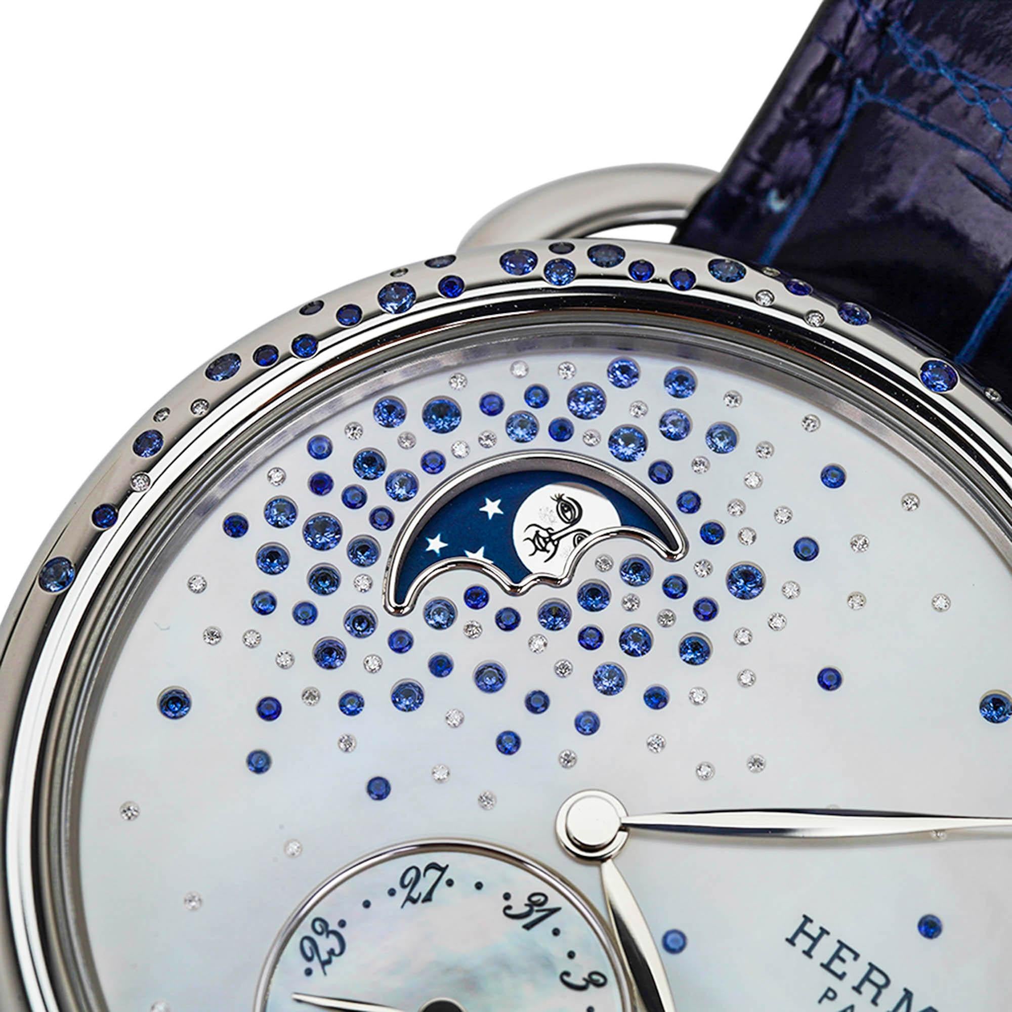 Mightychic offers an Hermes Arceau Petite Lune Watch featured in the 38 mm large model.
This beautiful diamond and sapphire set watch has gems sprinkled on the bezel and on the
mother of pearl dial.
The moon phase indicator has a blue background and
