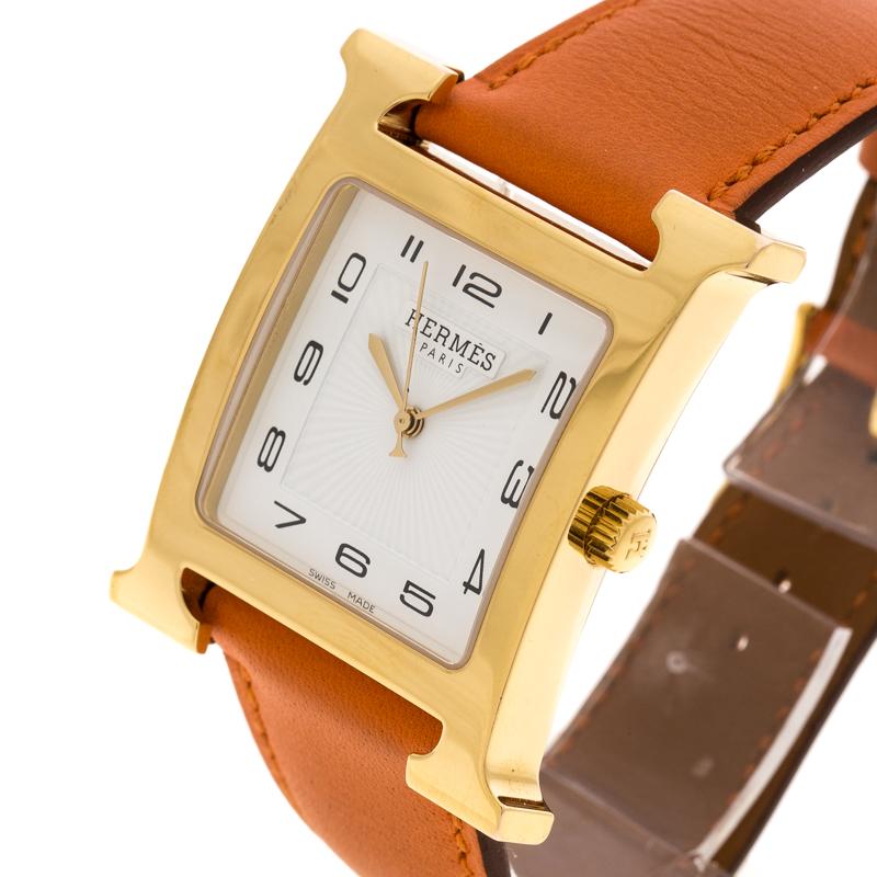 A vision of classic design, this Heure H GM watch from Hermes exudes quality and sophistication. The watch features the signature 'H' which has been beautifully transformed into a gold-plated stainless steel case held by an orange leather strap
