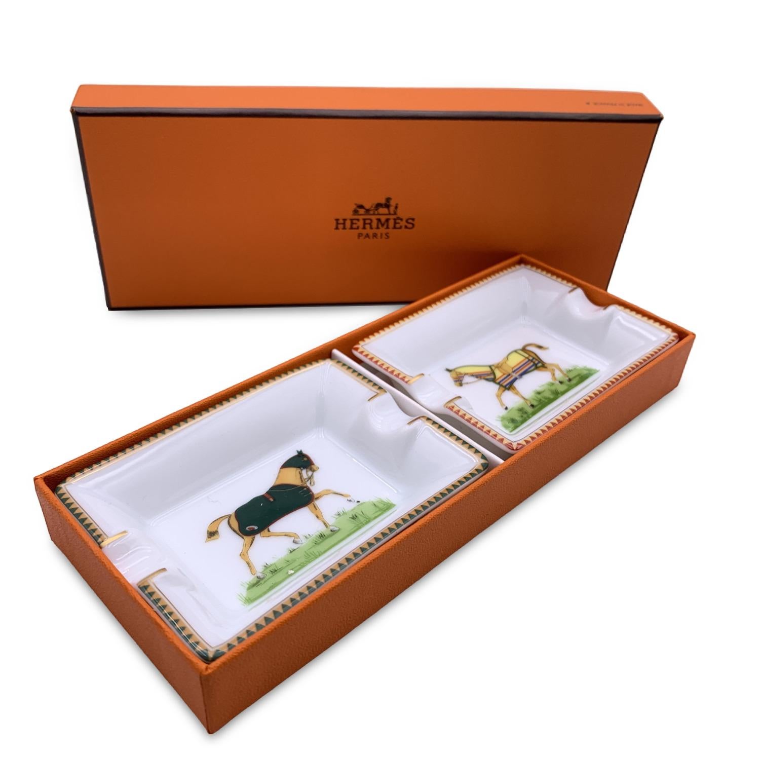 Hermes Vintage set of 2 mini ashtrays Rectangular shape. White porcelain decorated with a print of galloping horses in the centre of them. One horse wears a black blanket and one horse wears a yellow blanket with stripes. Each ashtray is marked with
