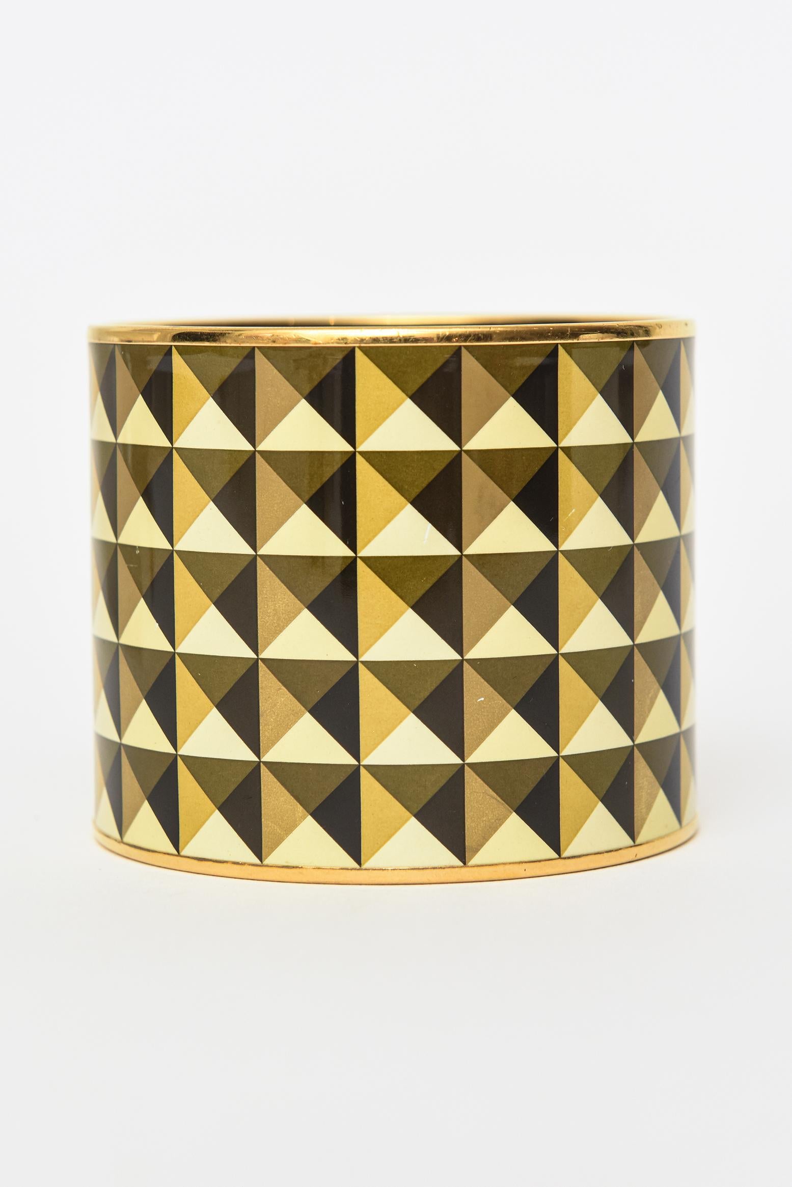 Ce fabuleux bracelet vintage Hermès à très large manchette émaillée présente un design géométrique. Le motif de demi-triangles en couleurs alternées de noir, jaune, or et brun olive est d'une beauté envoûtante. La bande métallique en laiton se