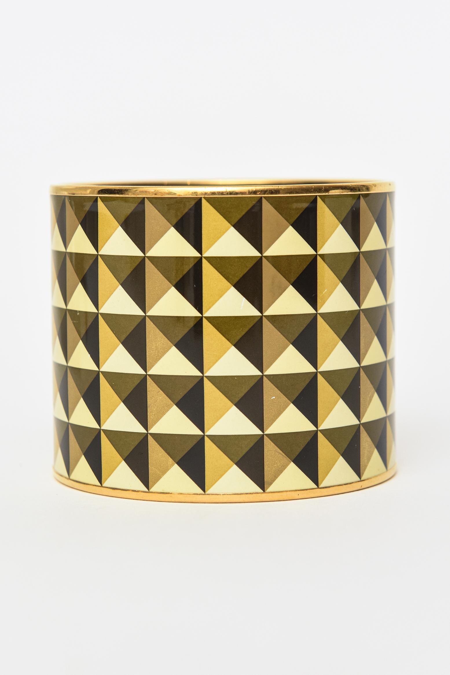 This fabulous vintage Hermes very wide cuff enameled bracelet is geometric in design. The pattern of half triangles in alternating colors of black, yellow, gold and olive brown make for a mesmerizing look. The brass metal banding is on top and