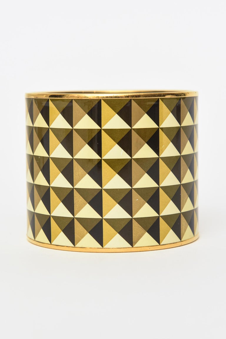 This fabulous vintage Hermes very wide cuff enameled bracelet is geometric in design.The pattern of half triangles in alternating colors of black, yellow, gold and olive brown make for a mesmerizing look. The brass metal banding is on top and