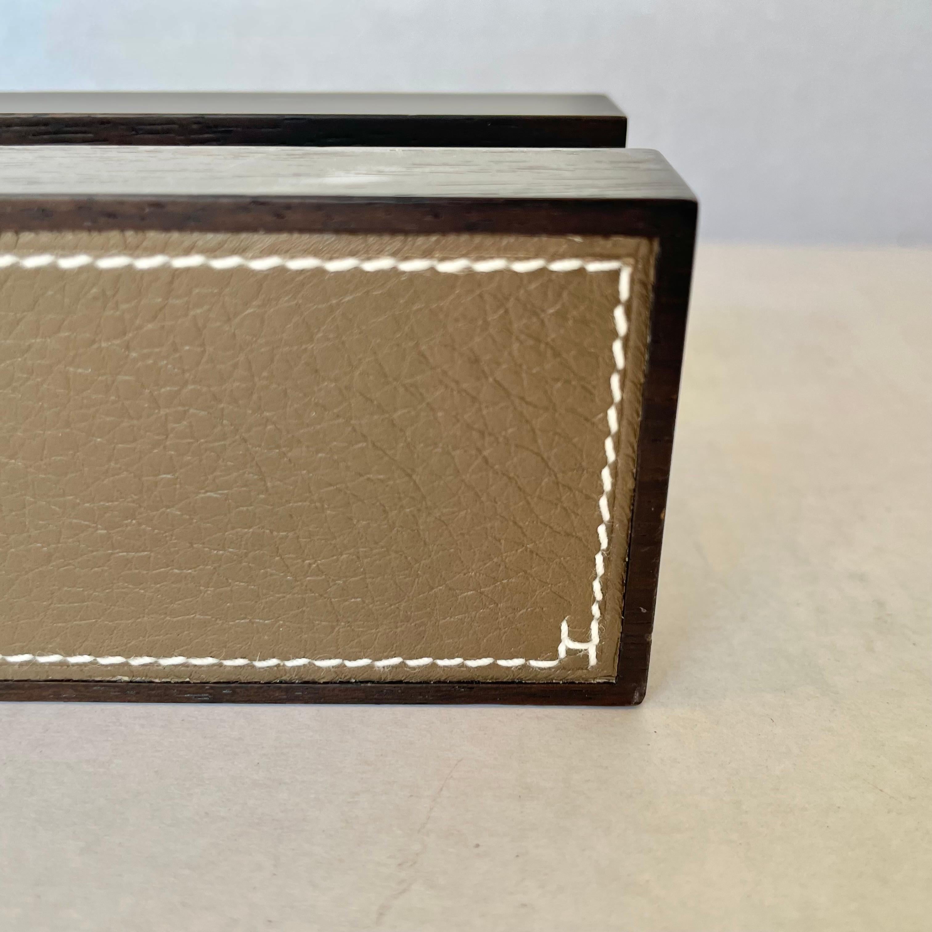 Hermès wood and leather business card holder. Made in France. Minimalist design. Dark hardwood body with taupe leather sides that feature contrast stitching as well as a small H stitched in the bottom right corner of one side. Stamped Hermes on the