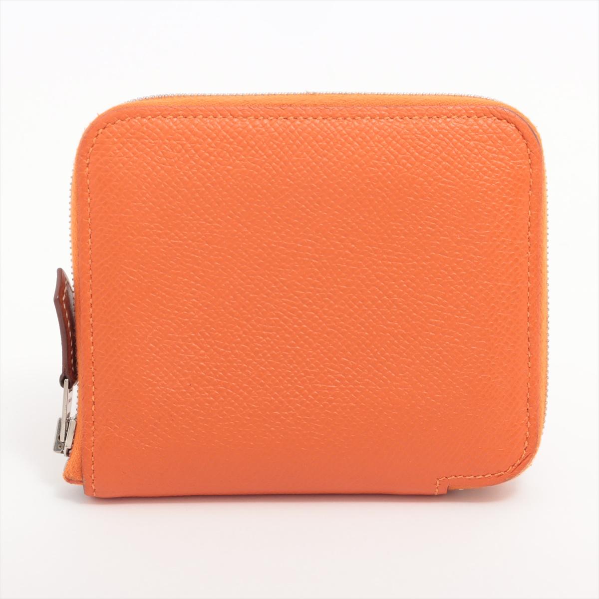The Hermès Zip Around Compact Coin Case in Orange a compact and vibrant accessory that effortlessly combines luxury with practical design. Meticulously crafted from smooth leather. The bold orange hue adds a touch of vibrancy to the sleek