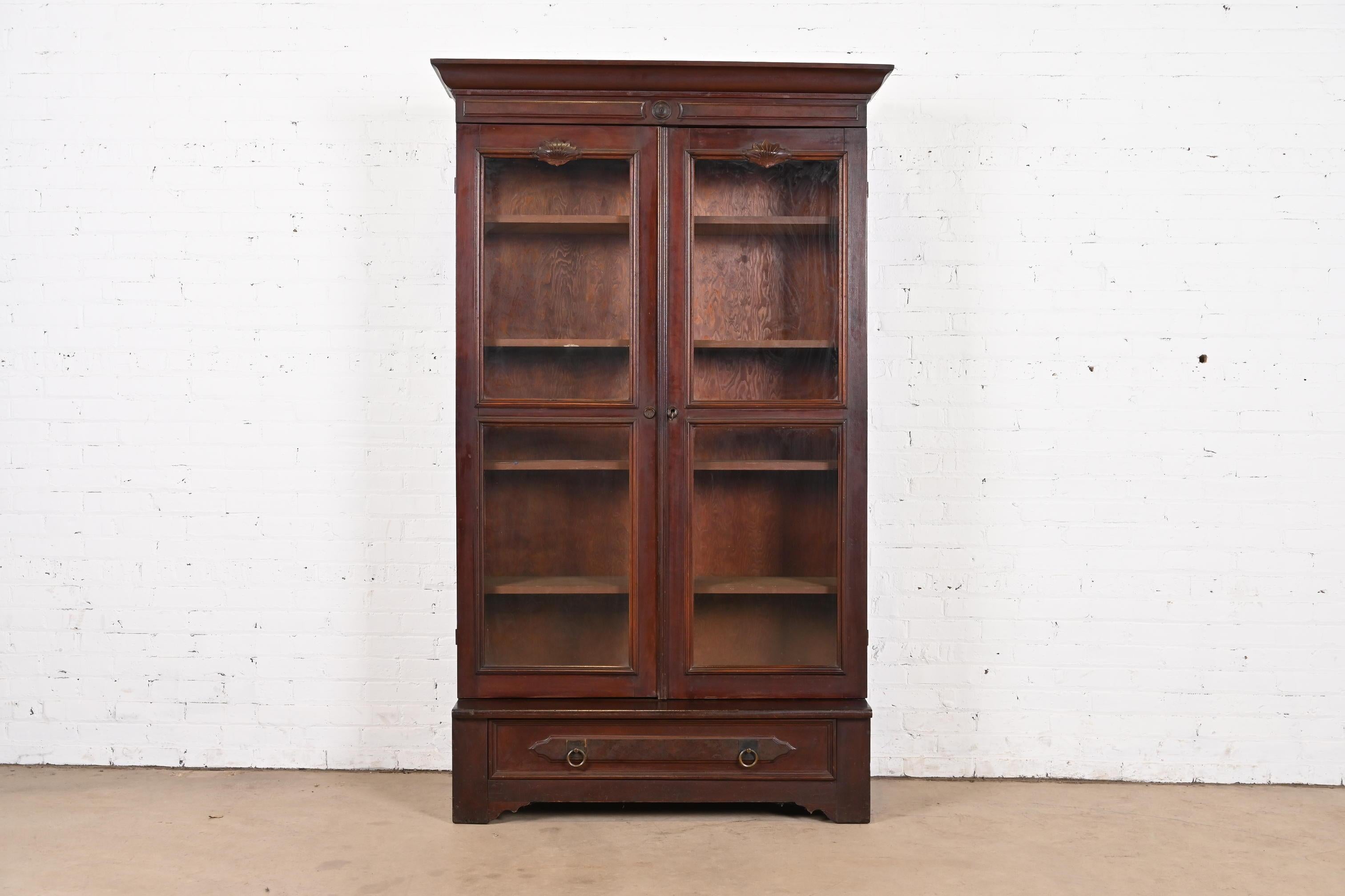 A beautiful antique Eastlake Victorian bookcase cabinet

In the manner of Herter Brothers

USA, Circa 1880s

Carved walnut, with burl wood panel on drawer, glass front doors, and original brass hardware.

Measures: 47.5
