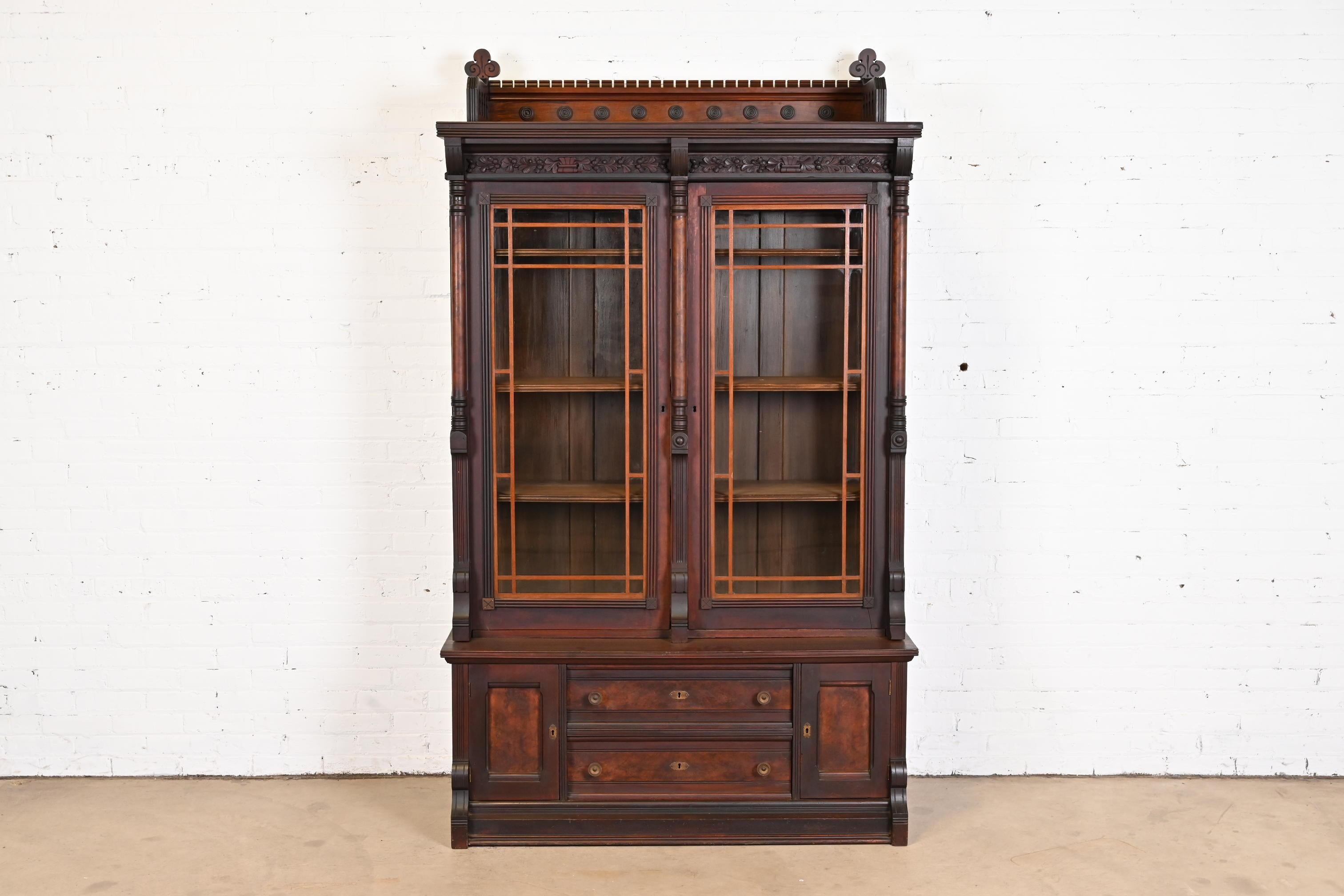 An outstanding antique Eastlake Victorian stepback bookcase

In the manner of Herter Brothers

USA, circa 1860s

Carved walnut, with burled walnut panels, mullioned glass front doors, and brass hardware.

Measures: 50