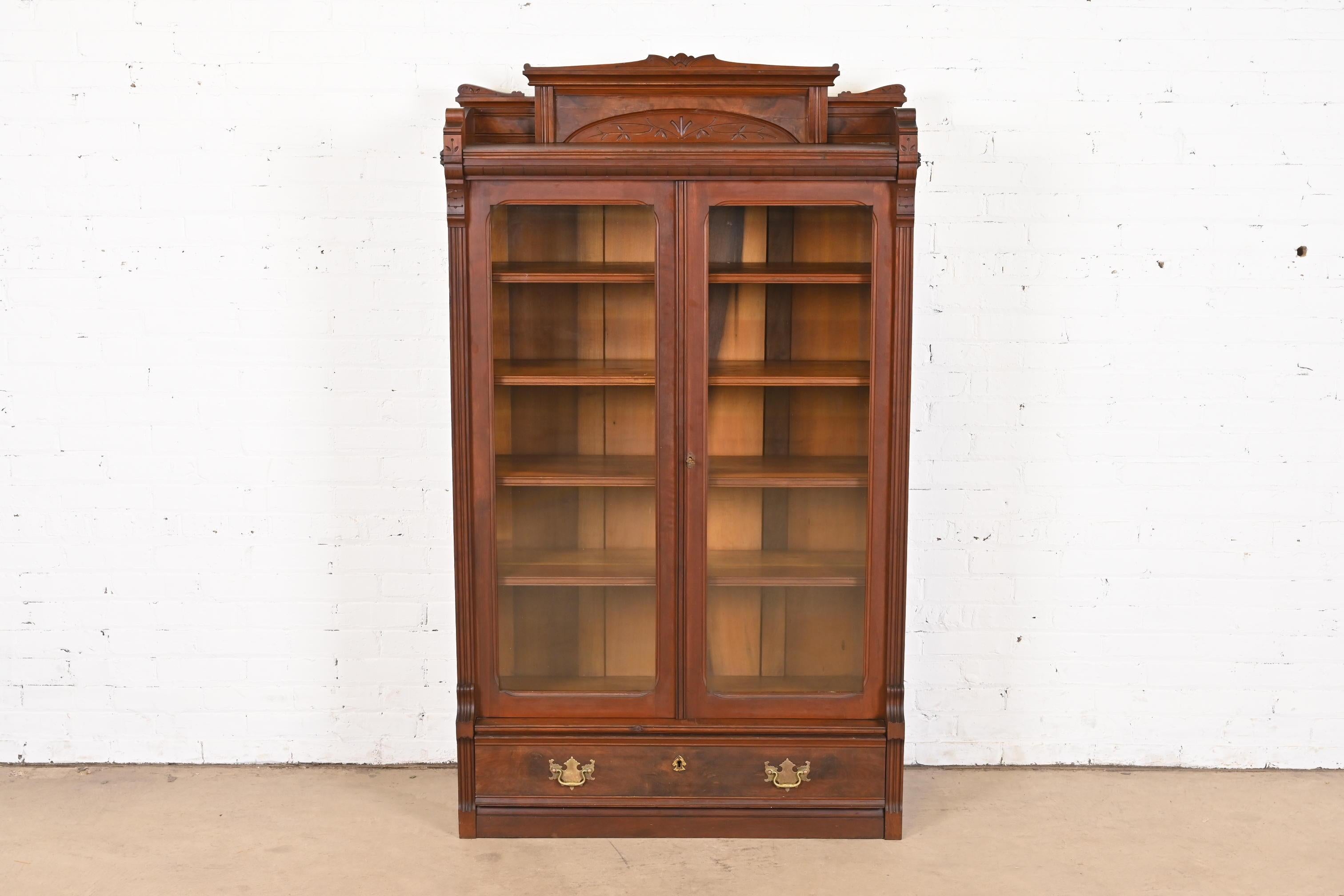 An outstanding antique Eastlake Victorian bookcase cabinet

In the manner of Herter Brothers

USA, Circa 1860s

Carved walnut, with burled walnut panels, glass front doors, and brass hardware.

Measures: 38.75