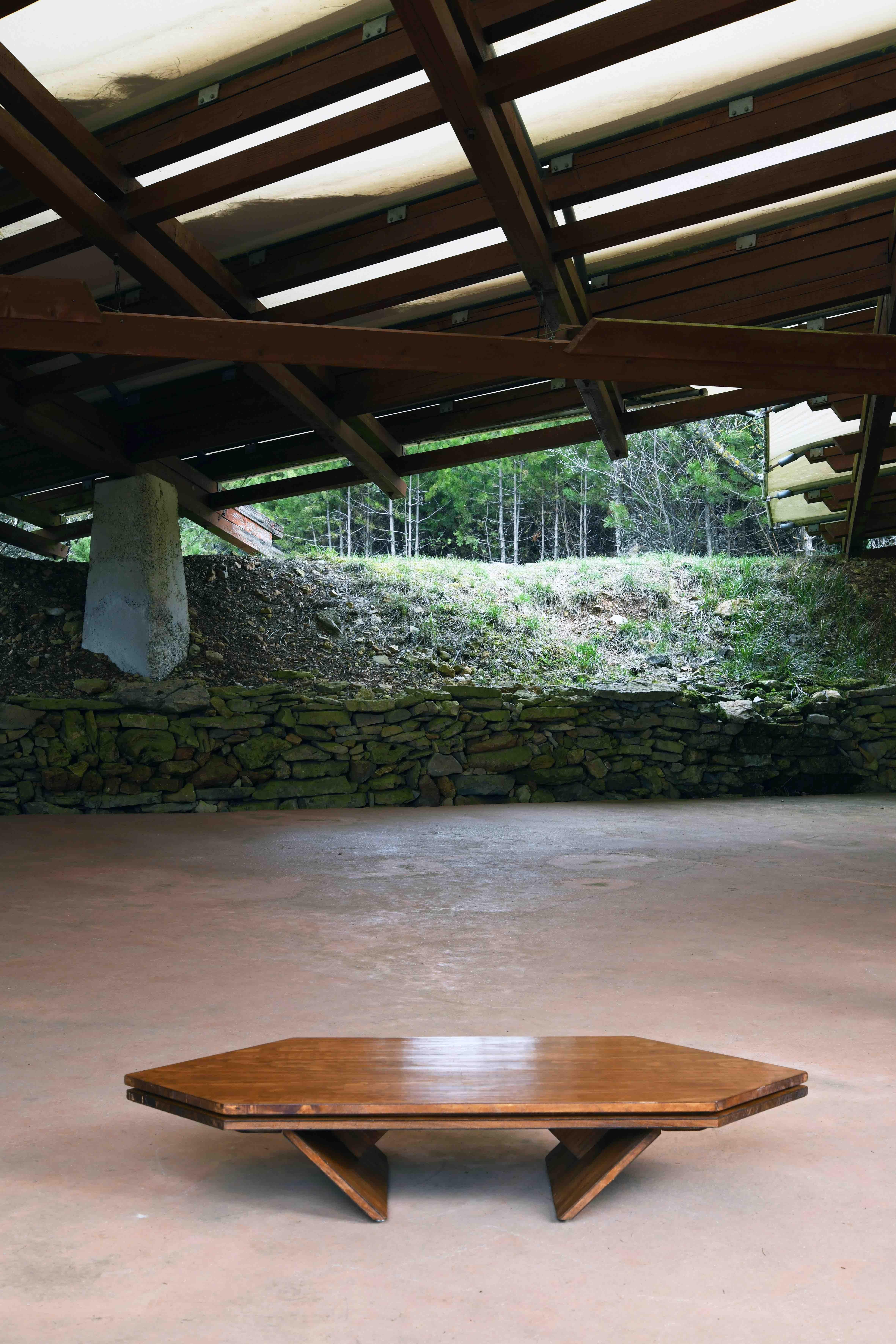 Low hexagonal coffee table made of Oregon pine on structured wood. The angular table features 45 degree points on both ends of the table top with similar angled feet pointing inward, extending the top and bottom to an almost 135 degree angle.