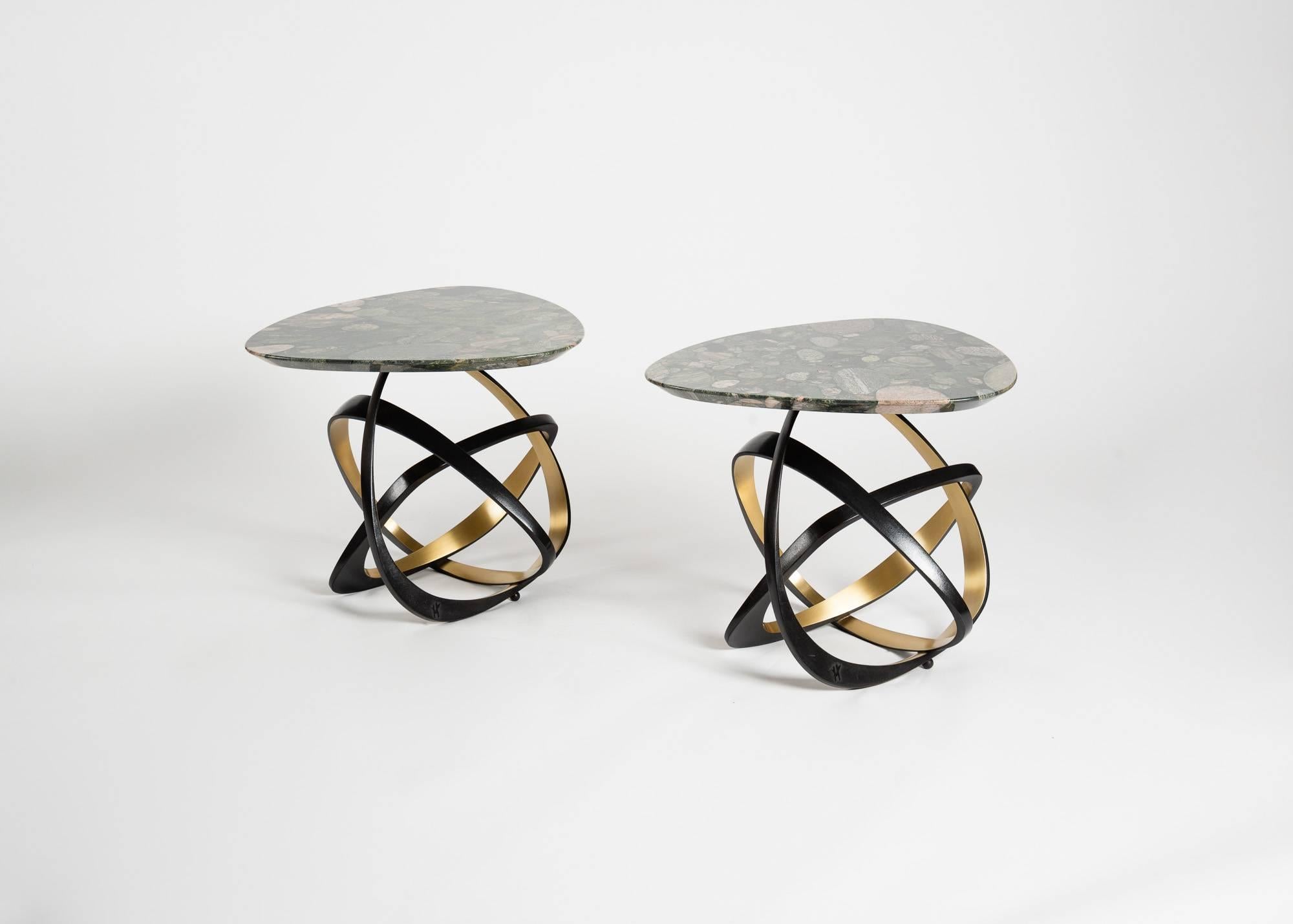 This contemporary table features a marinace marble top set with cross-sectioned stones, as well as three lopsided bronze supports, each with a gilt bronze facet. These dynamic metal rings provide a light, airy aesthetic and successfully evince space