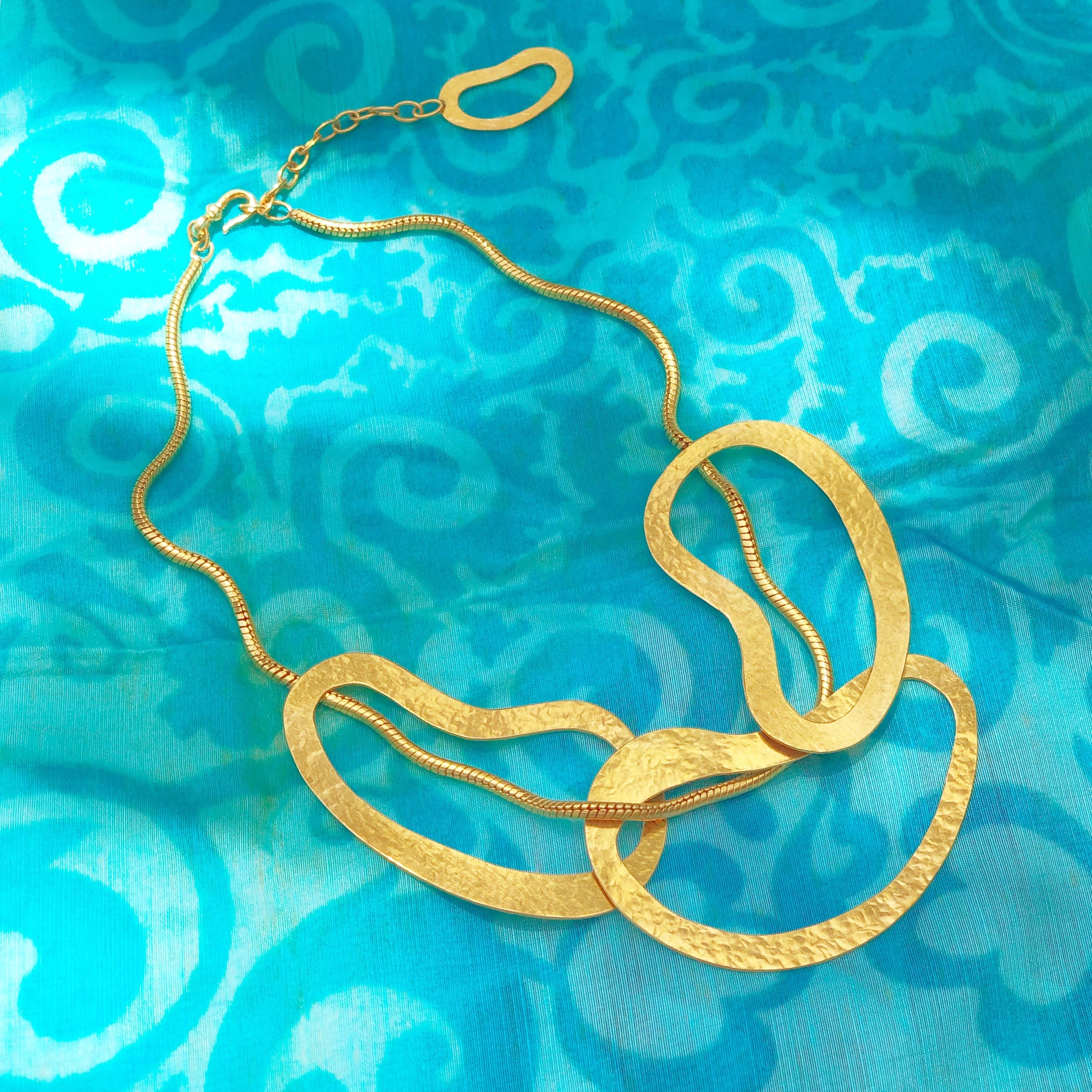 Exquisite gilt abstract contemporary statement necklace by designer Herve van der Straeten. Hammered gold-plated brass rings intertwine with a sleek serpentine rope chain in this unique work of wearable architectural art!  A wonderful addition to