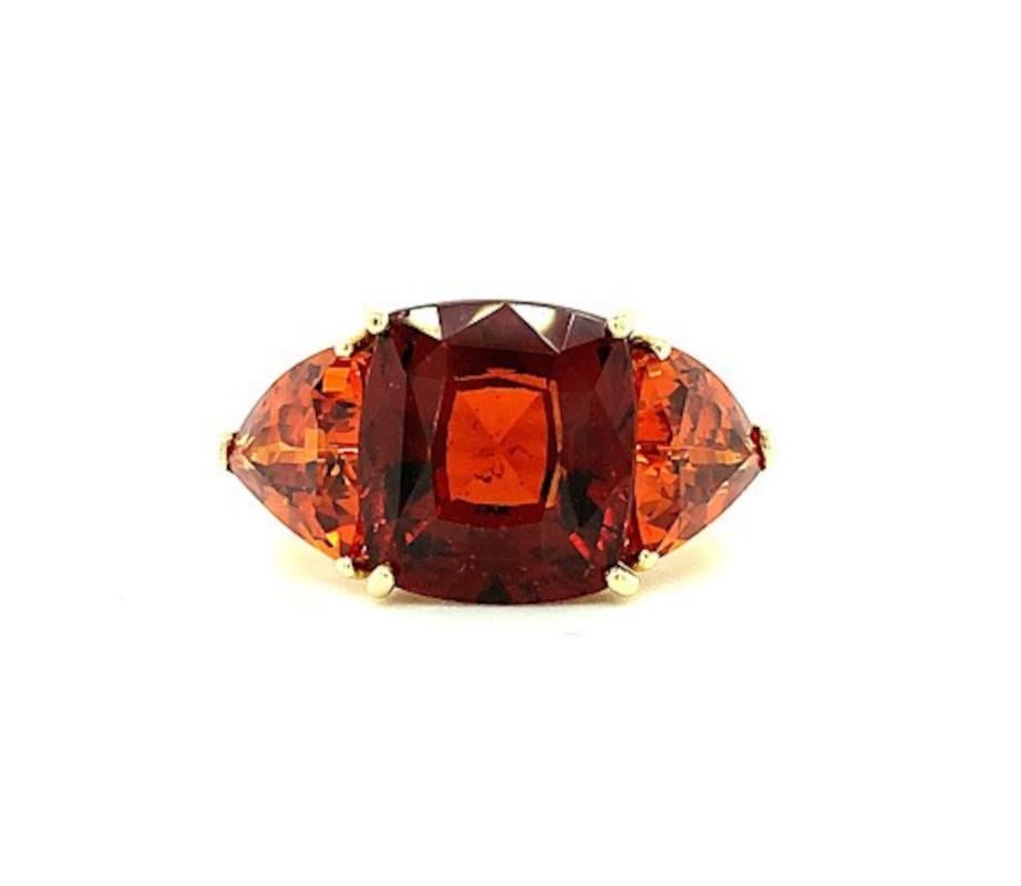 This eye-catching ring features a large 7.20 carat cushion-cut hessonite garnet and two brilliant spessartite garnet sides stones set in 18k yellow gold. The center gemstone has a rich, reddish orange, 