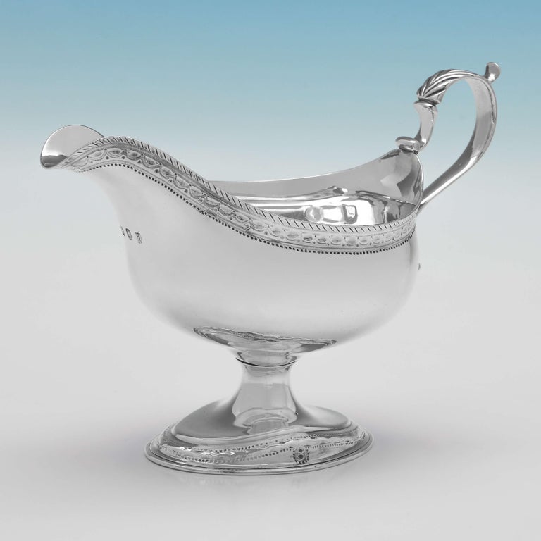 Hallmarked in London in 1784 by Hester Bateman, this striking, George III, antique silver pair of sauce boats, are in the Neoclassical style, standing on pedestal feet, and oval in shape, featuring acanthus detailed scroll handles, and bright cut