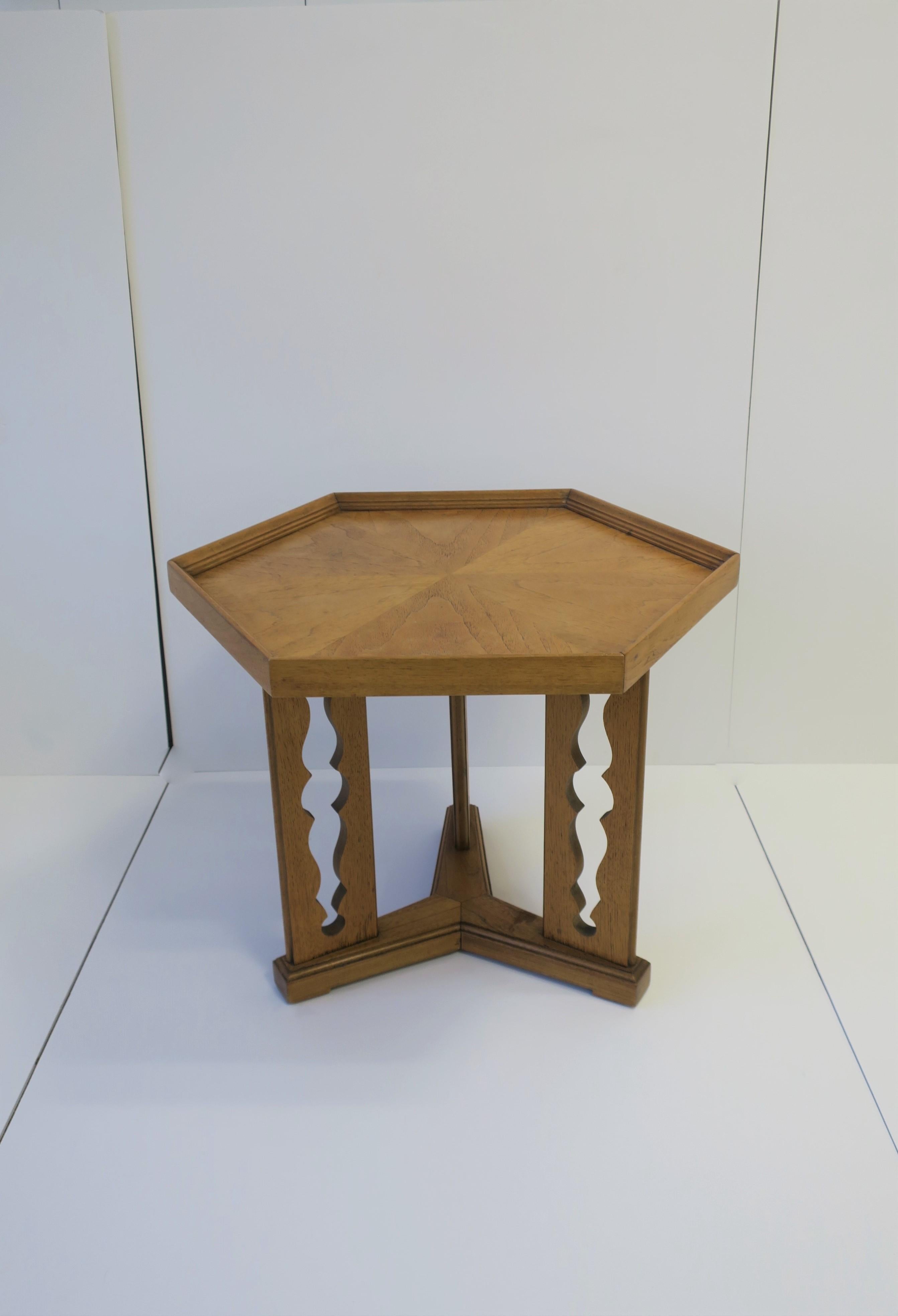 A hexagon top wood side or end table 'Esperanto' by Drexel with decorative base. The hexagon shape tabletop is a nice alternative to round, and 'cut-out' base adds a nice decorative element. Hue is a medium 'blonde' as show in images. Maker's mark