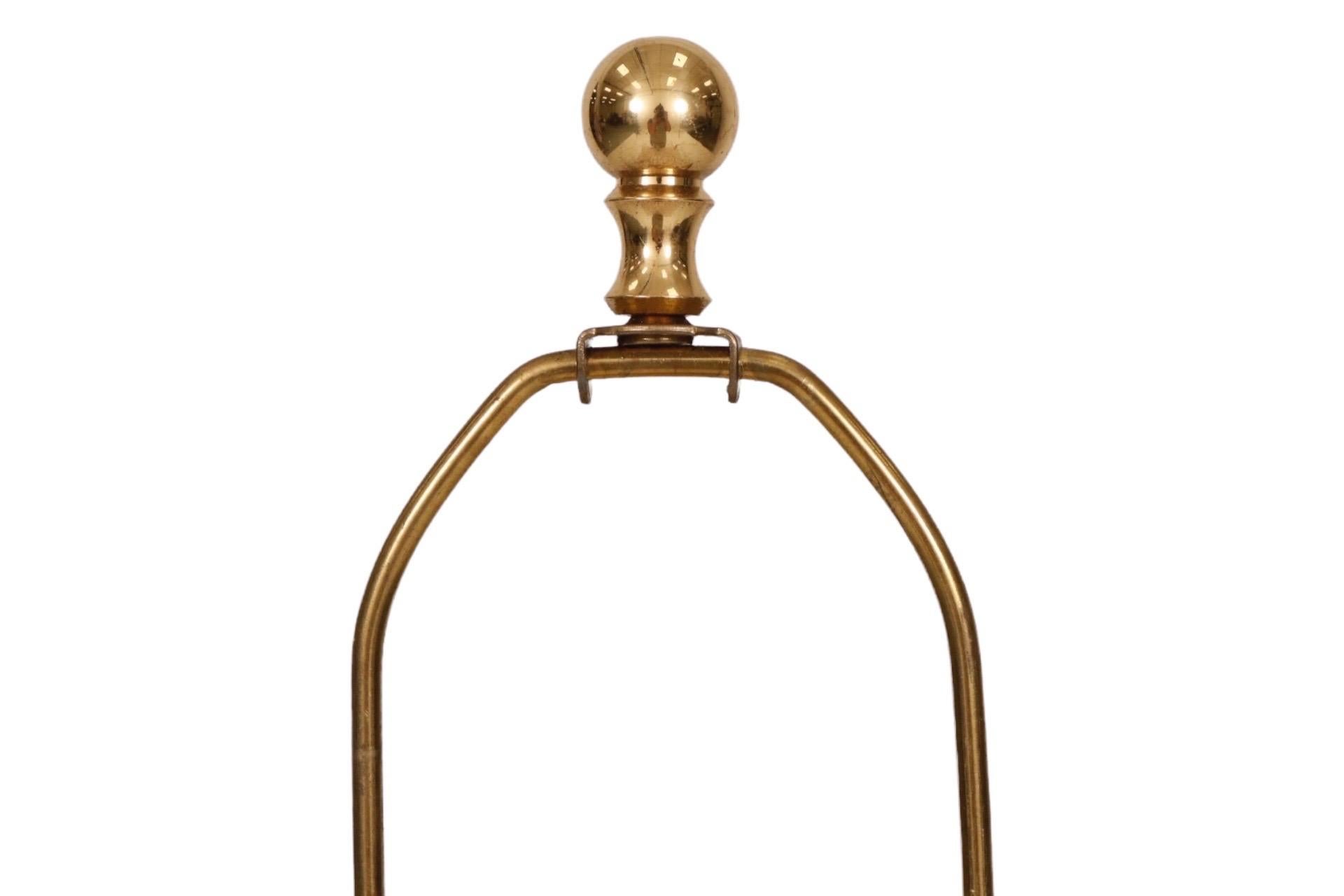A tall ceramic table lamp in yellow. A simple arched base supports an hexagonal body and rounded neck. The harp is topped with a brass ball finial. Measures 21.5