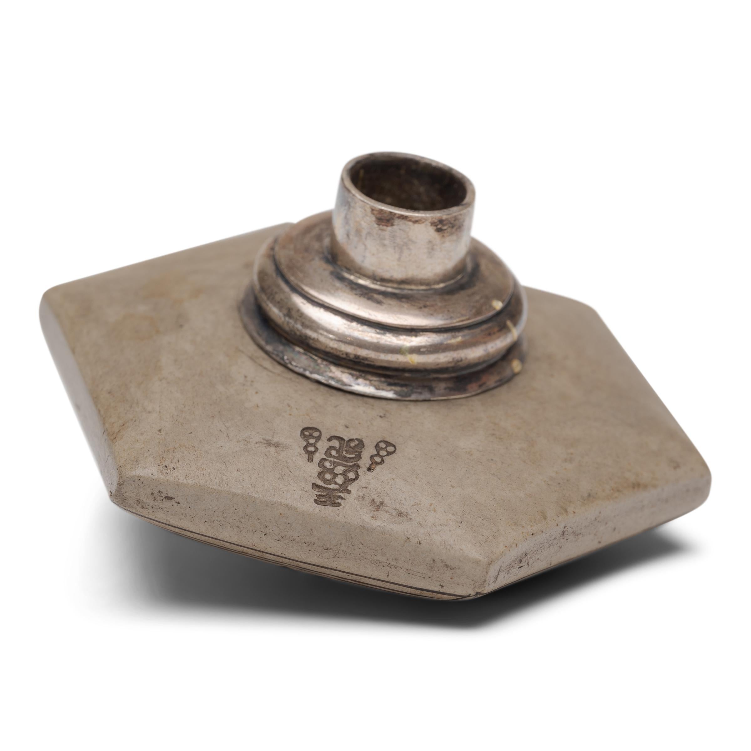 This unusual object is an early 20th century opium pipe bowl, beautifully sculpted of ceramic to a hexagonal disc form and fitted with a white brass collar. The top of the bowl is decorated with the characters for longevity and good fortune, drawn