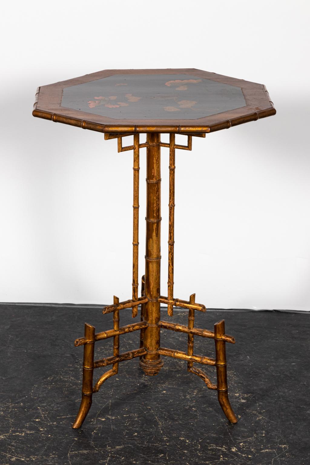 Hexagonal faux bamboo side table with a painted tabletop featuring flowers and butterflies. Please note of wear consistent with age including paint loss, finish loss, and chips as seen on the base and corners of the tabletop.
