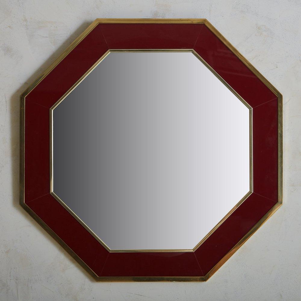 An elegant French hexagonal shaped wall mirror in a deep burgundy hue with a lacquered finish. This piece has a patinated brass trim, which contrasts beautifully with the burgundy frame. Sourced in France, 1970s.

A matching console is table is