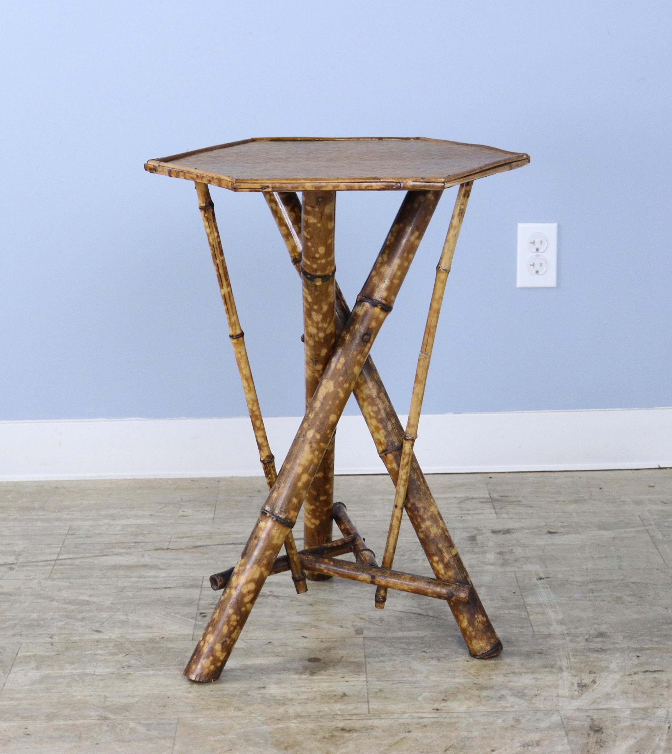An antique English bamboo side table, with tripod legs and additional decorative supports. Attractive details on all sides. The top is made of tightly woven rattan that is in very good condition. The bamboo, vividly painted, is in good sturdy