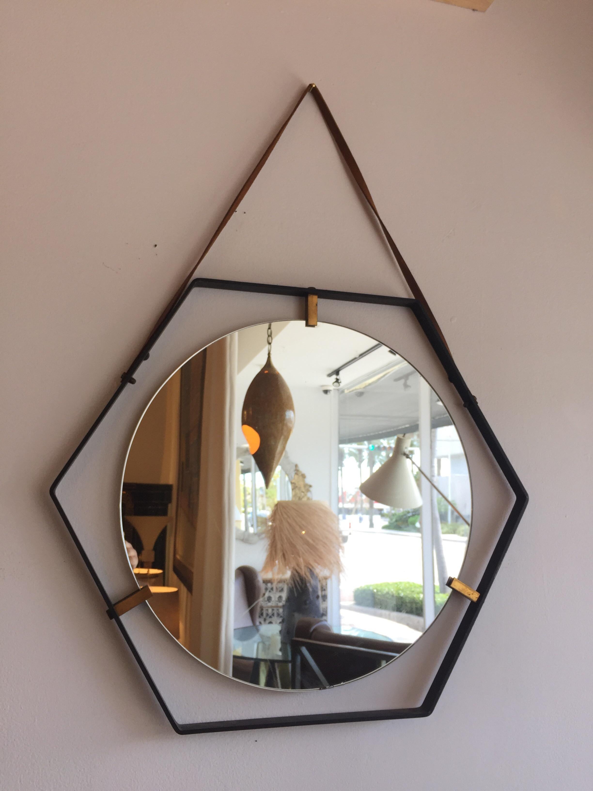 A wonderful round mirror floating in a flat metal hexagonal frame and hung by a leather strap. Designed by Santambrogio & De Berti in the 1950s with brass hardware.