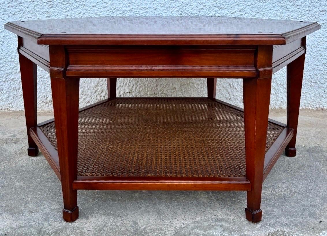 Elegante mesa de centro hexagonal vintage fabricada en madera maciza con un cálido acabado caoba satinado. El tablero presenta un refinado borde enmarcado y una carpintería visible que resalta la artesanía de la pieza.
Su nivel inferior está