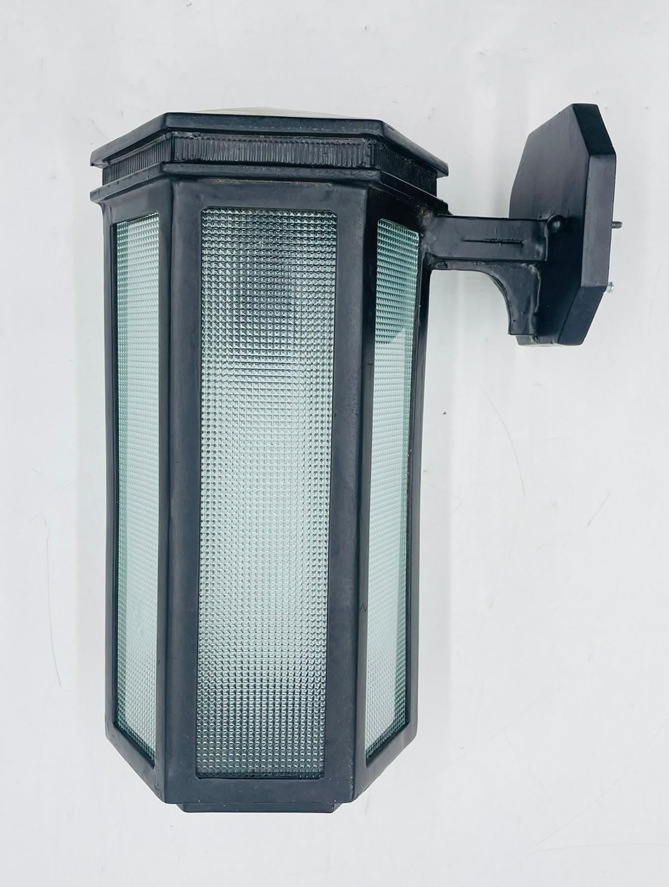 A custom-crafted wall sconce by Steven Handelman Studios, dated June 2001, combining classic form with durable materials. This handcrafted fixture features a hexagonal body made of black wrought iron and textured prismatic glass panels, offering a