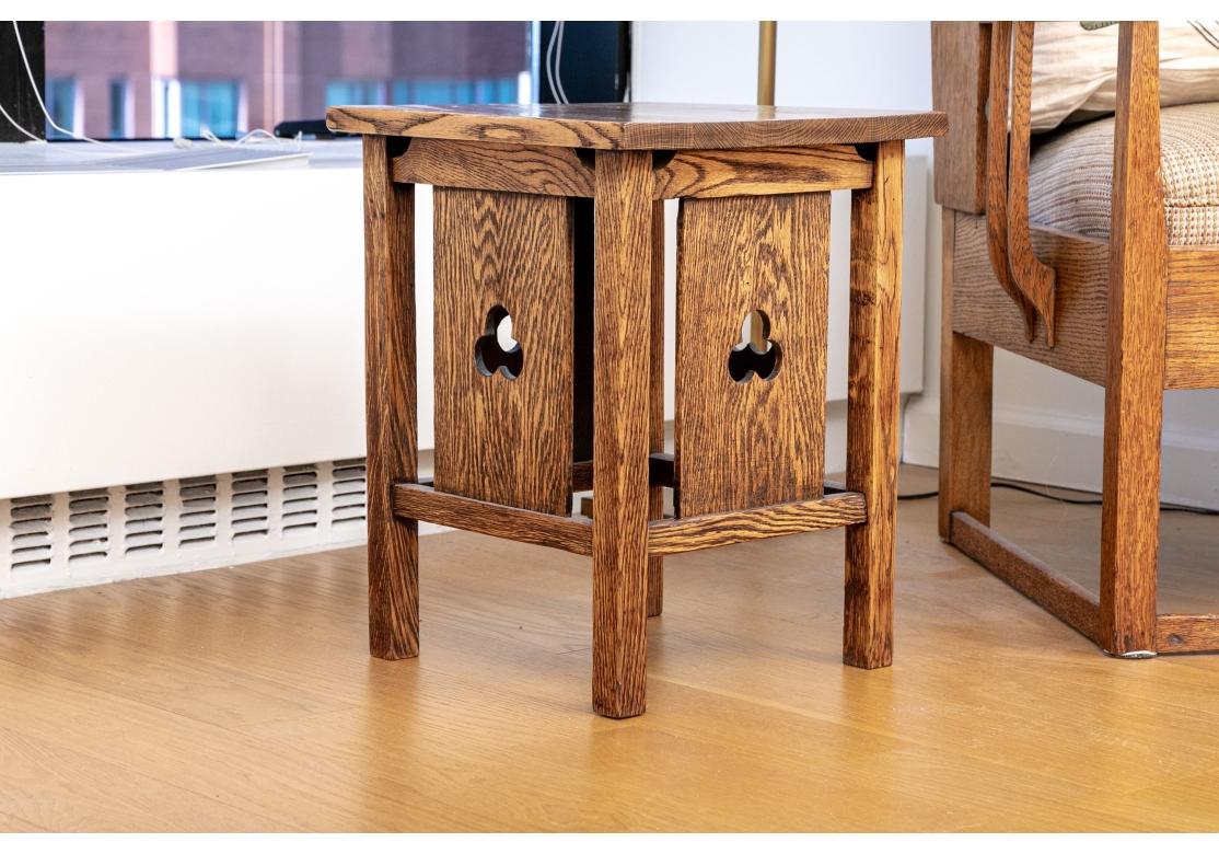 The oak side table having a square form and paneled sides with trefoil cutouts along the box stretcher, rests on straight legs.

Dimensions: 14 1/4