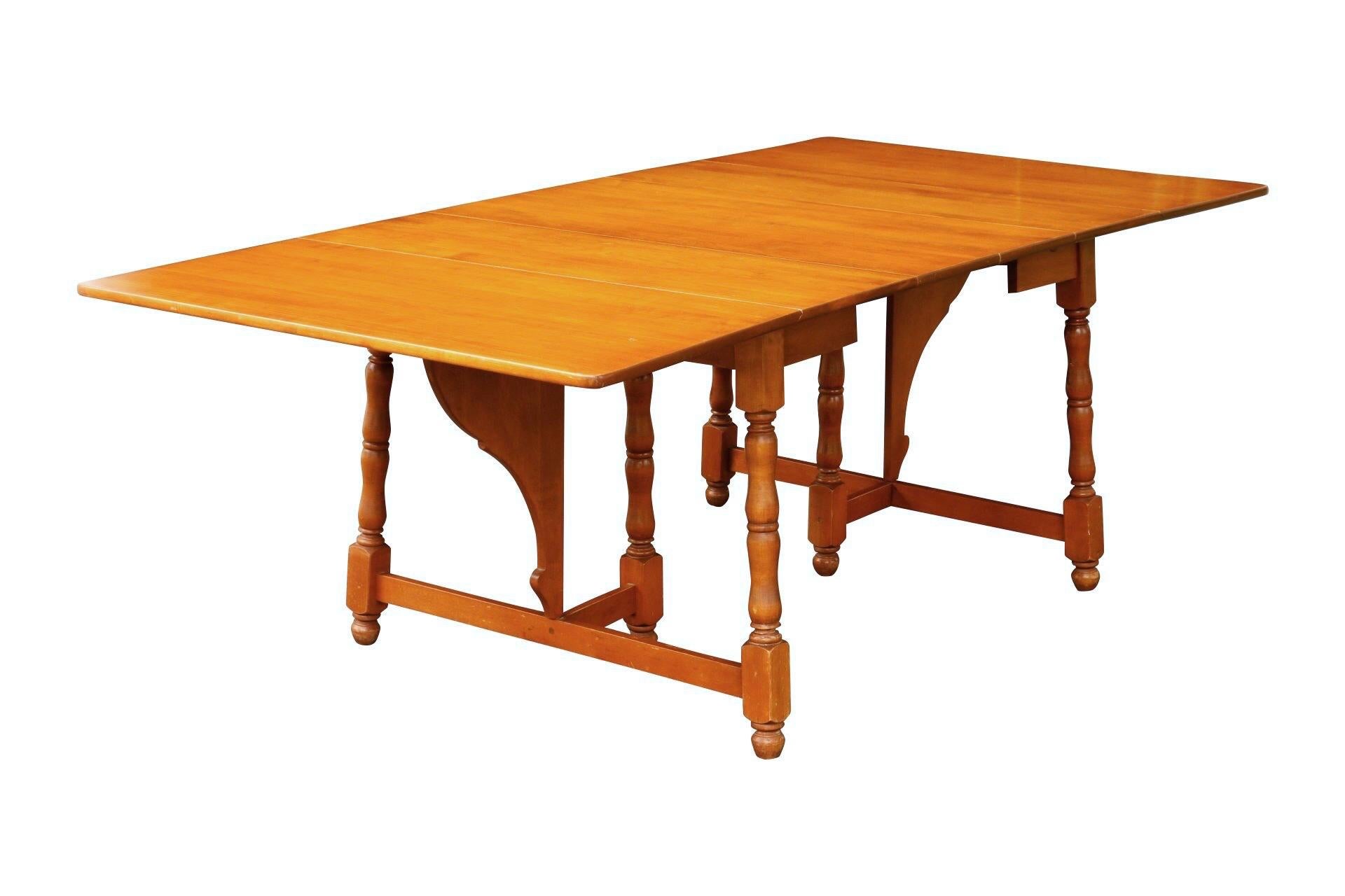 A traditional style drop leaf dining table made by Heywood Wakefield. The drop leaves lift, supported with butterfly brackets to form a rectangular table that seats six. The table extends with two leaves to comfortably seat eight. Six turned legs