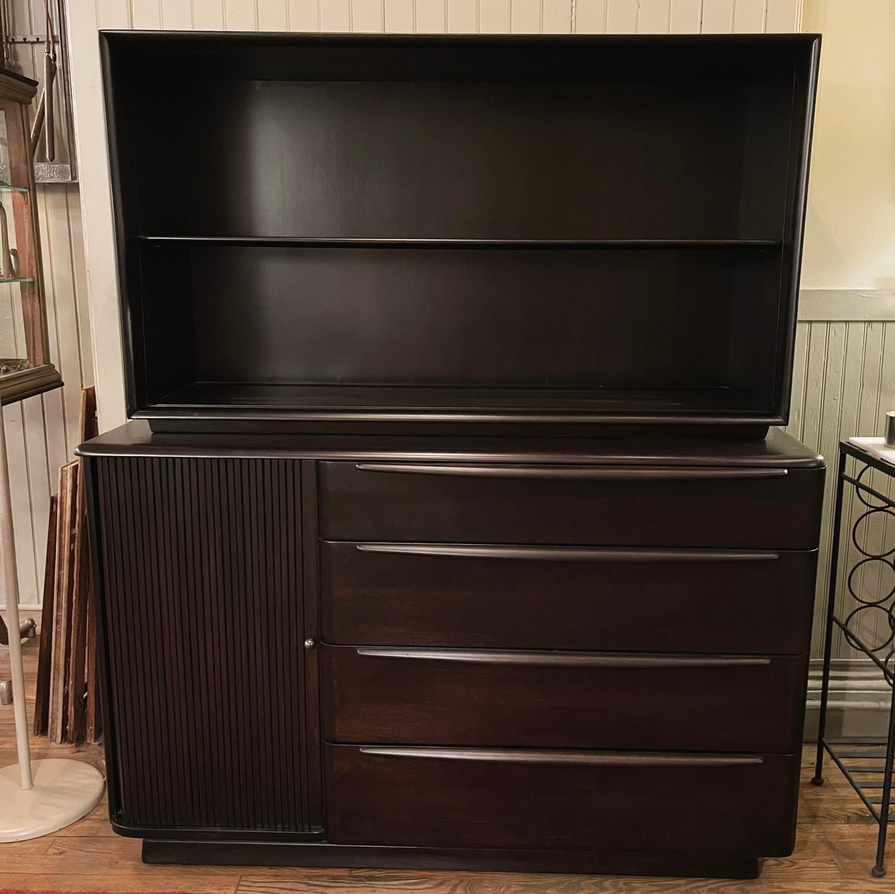 Iconic, art deco inspired, Mid-Century Modern, ebonized maple, two piece, credenza hutch by Heywood Wakefield Co. features a bottom credenza with left side tambour front compartment and three drawers and top hutch with open shelving. The top portion