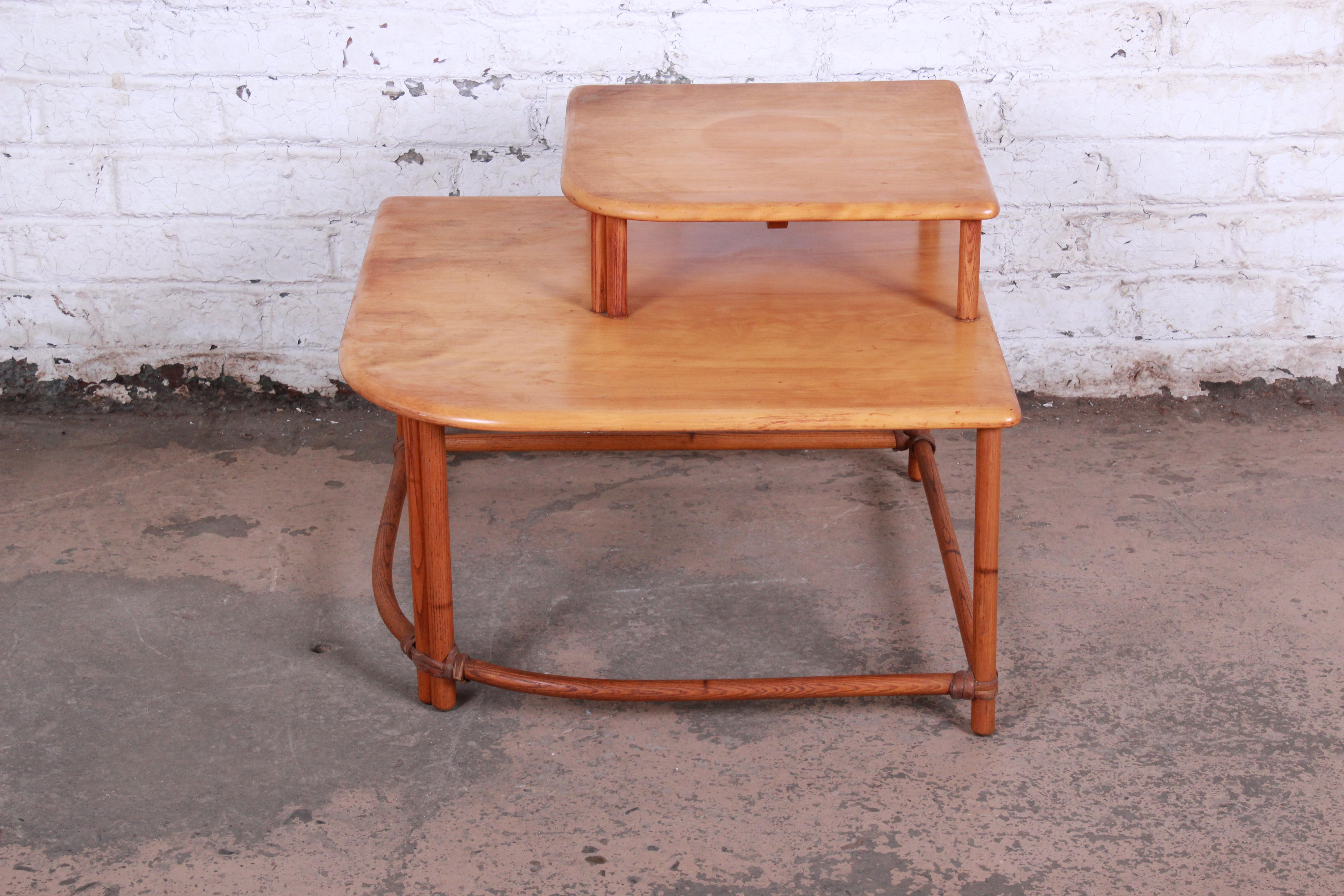 A nice and unique Mid-Century Modern Hollywood Regency style end table from the Ashcraft line by Heywood Wakefield. The end table features a gorgeous bent rattan frame and a two-tiered top with ample area to hold numerous items. The table is in