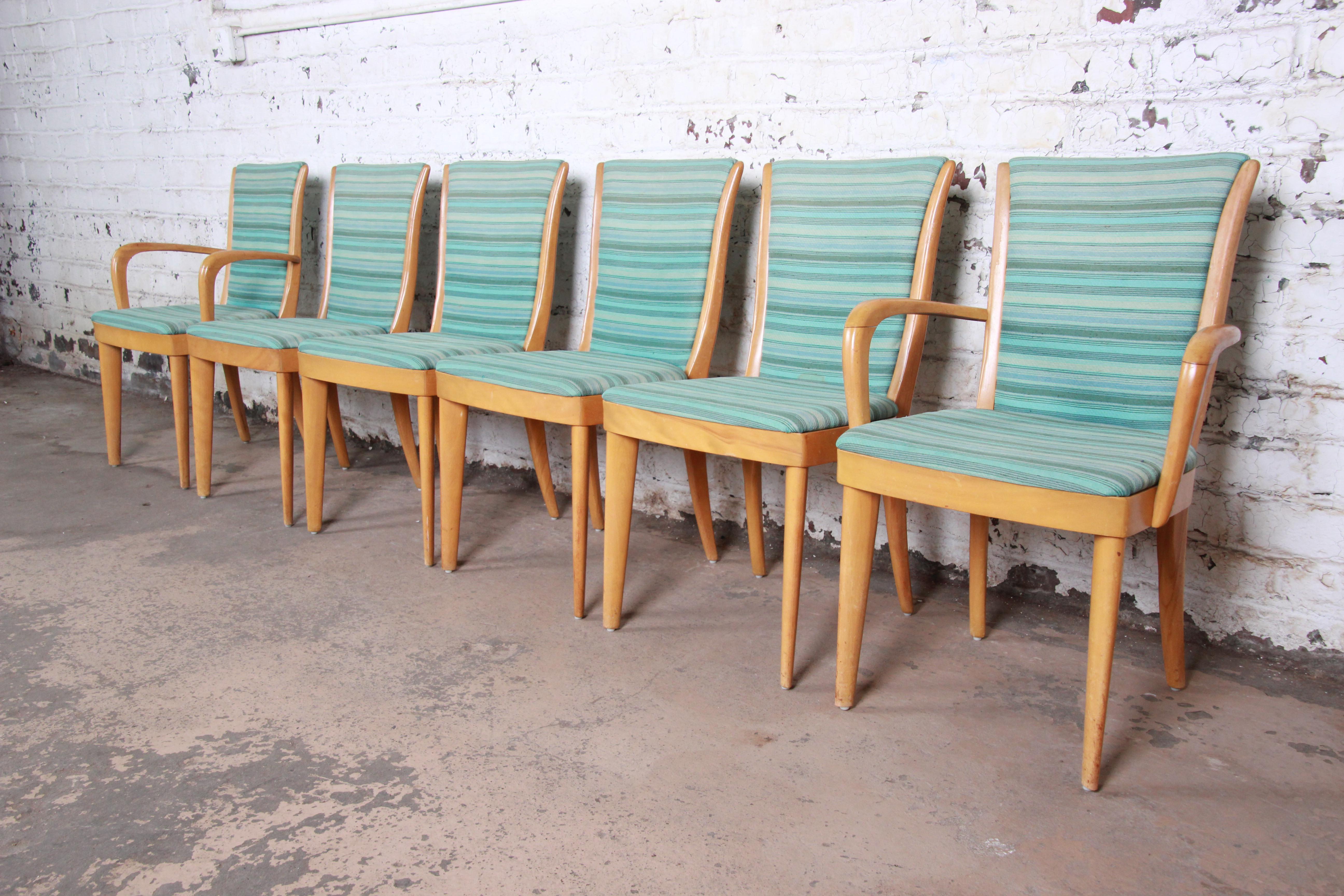 A gorgeous set of six mid-century modern dining chairs by Heywood-Wakefield. The set includes two captain armchairs and four side chairs. The chairs feature solid sculpted maple frames and vintage striped upholstery in blues and greens. The original
