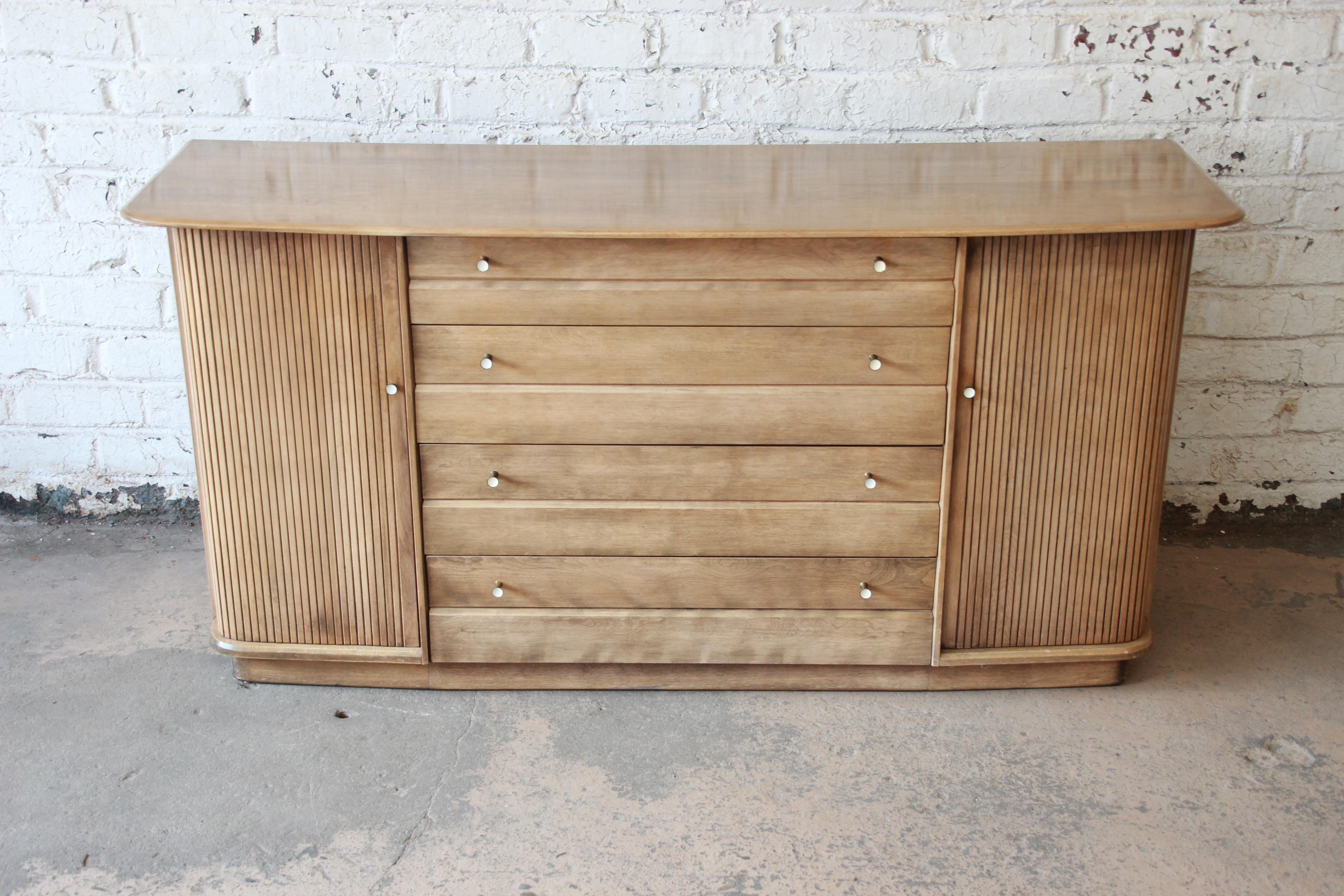 A very nice solid maple sideboard buffet or credenza by Heywood Wakefield. The sideboard features beautiful wood grain and clean midcentury lines. It offers ample room for storage, with two shelved cabinets behind tambour doors on each side and four