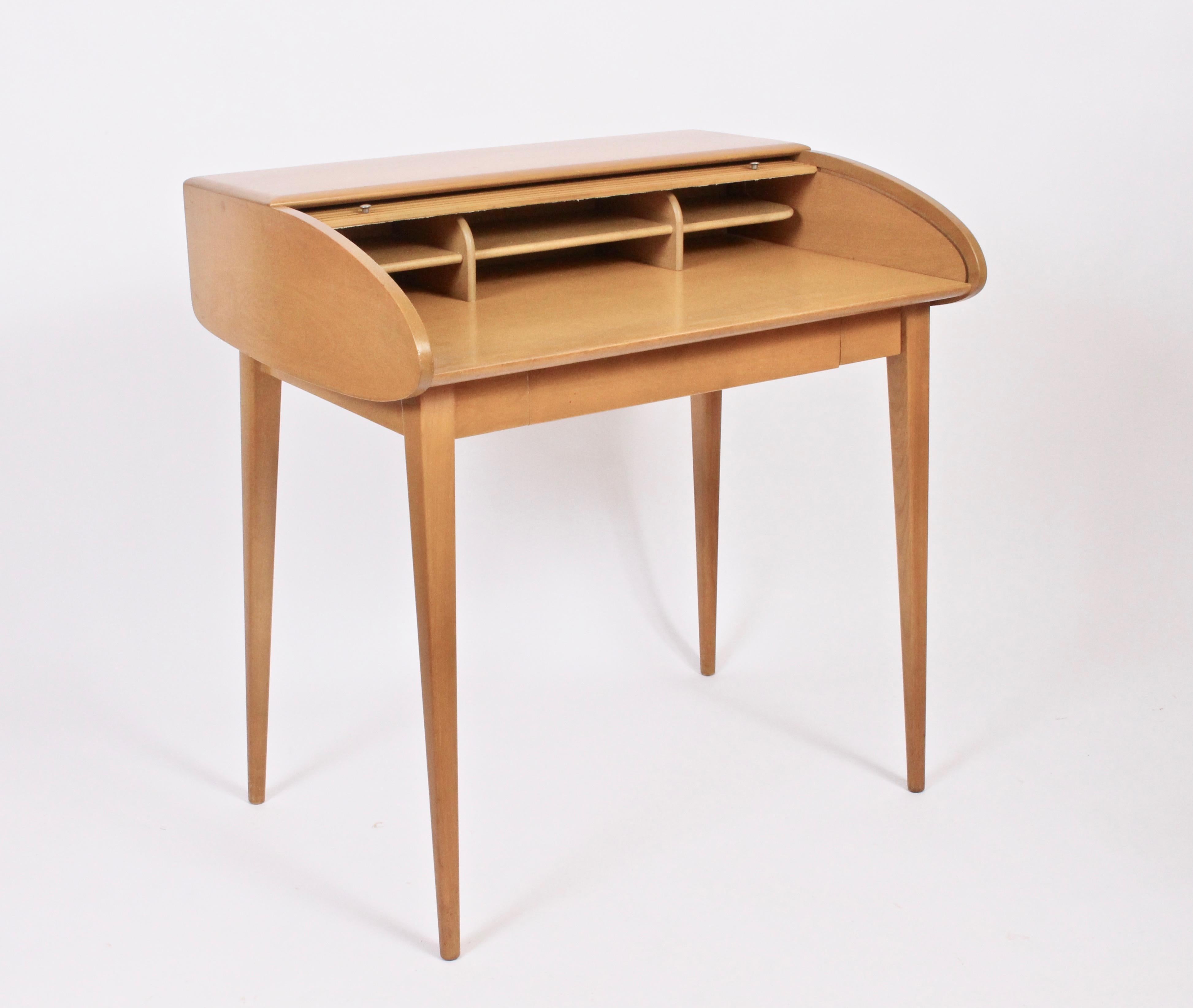 Classic American Mid Century Heywood-Wakefield Petite Birch Roll Top Desk. With finished back.  Featuring six interior compartments.  Legs attach and detach with wingnuts. Amber finish. Rarity. Sleek. Storage. Small footprint. Eagle burn stamp